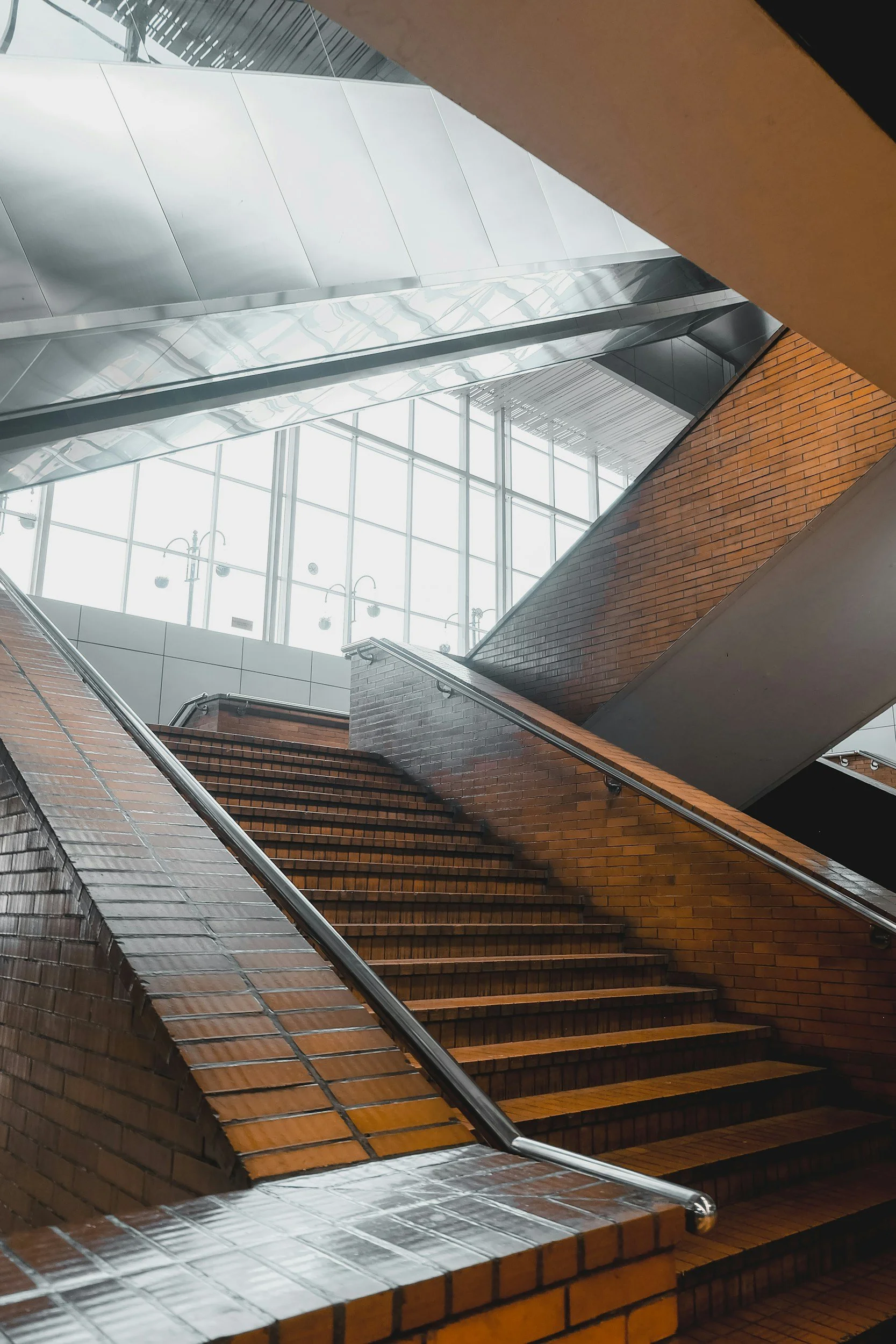 Indoor staircase with brick walls, metal handrails, and large windows with a metal ceiling above.