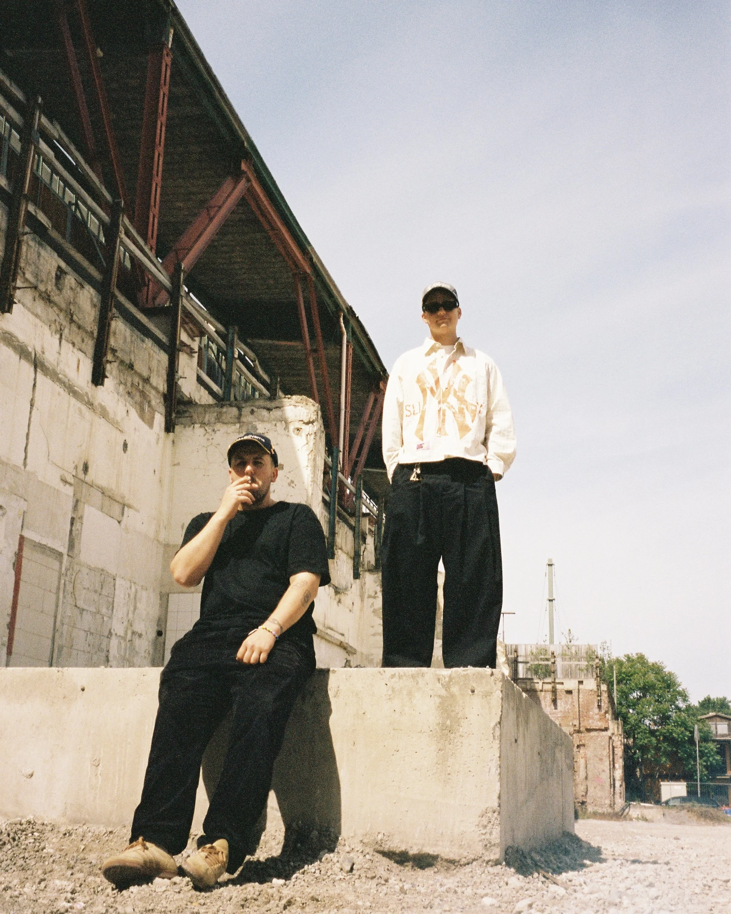 Zwei Männer auf einer erhöhten Plattform vor einem alten Gebäude bei sonnigem Wetter.