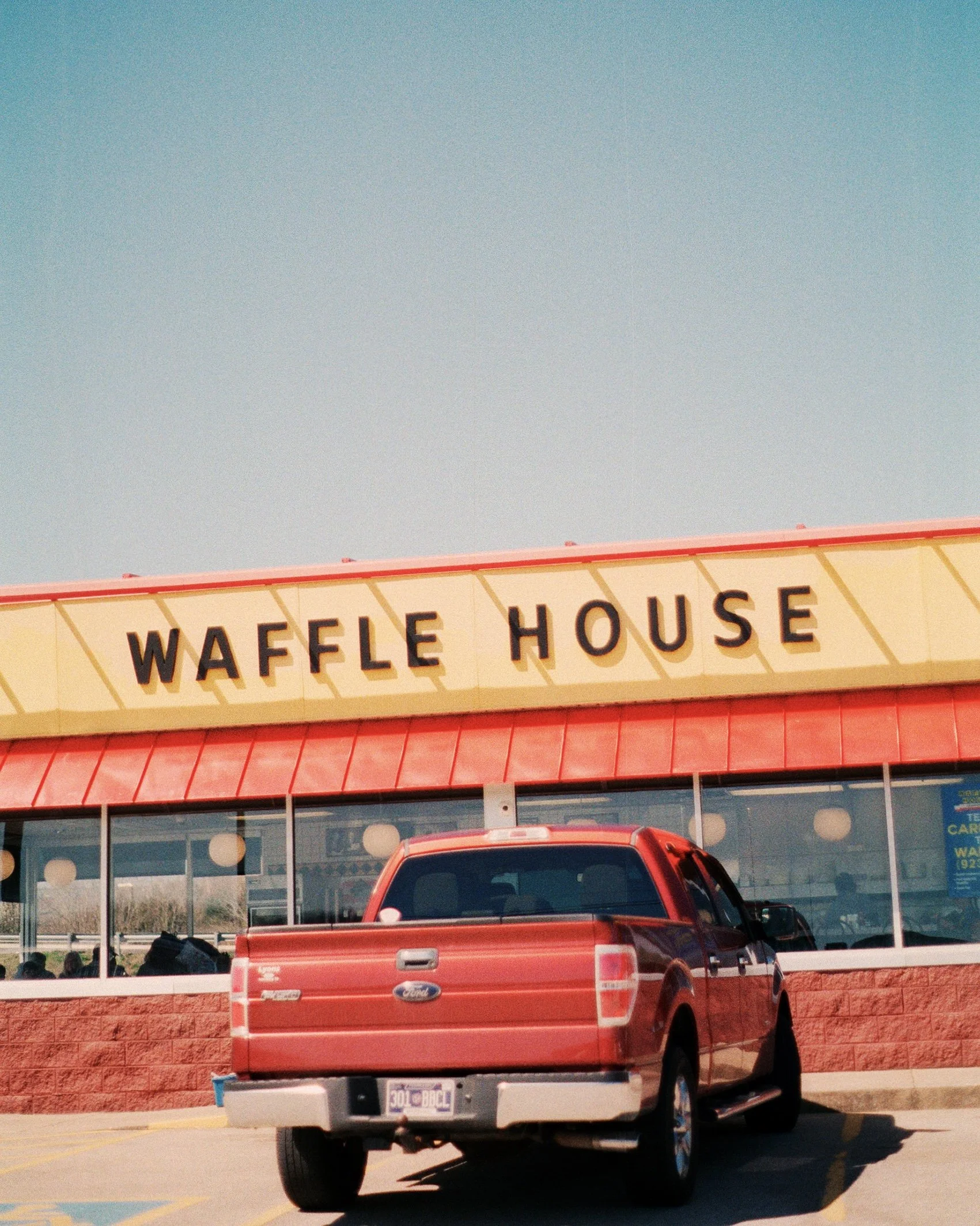 Ein rotes Pickup-Fahrzeug parkt vor einem Waffle House Restaurant mit gelbem und rotem Dach, großes gelbes Schild mit schwarzen Buchstaben und einem großen Fenster.