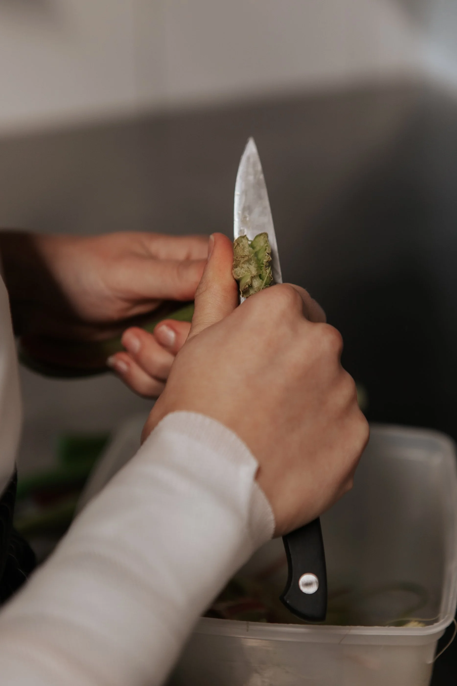 Gros plan des mains d'une personne coupant un fruit ou légume avec un couteau dans un récipient