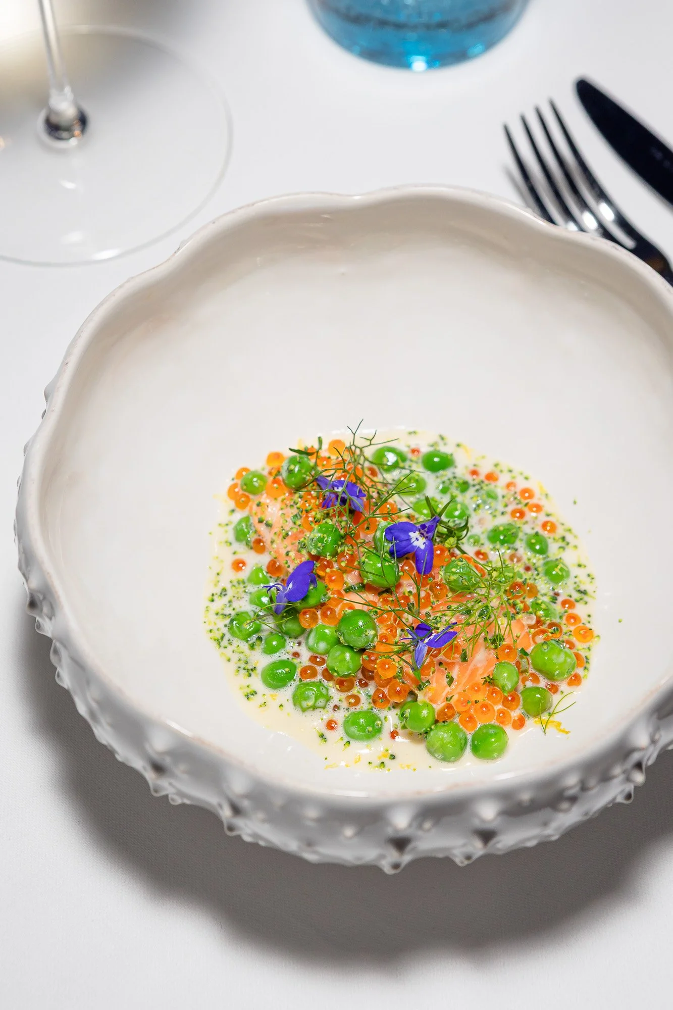 Plat de saumon avec pois, œufs de calmar, et fleurs violettes sur une sauce crémeuse dans une assiette blanche