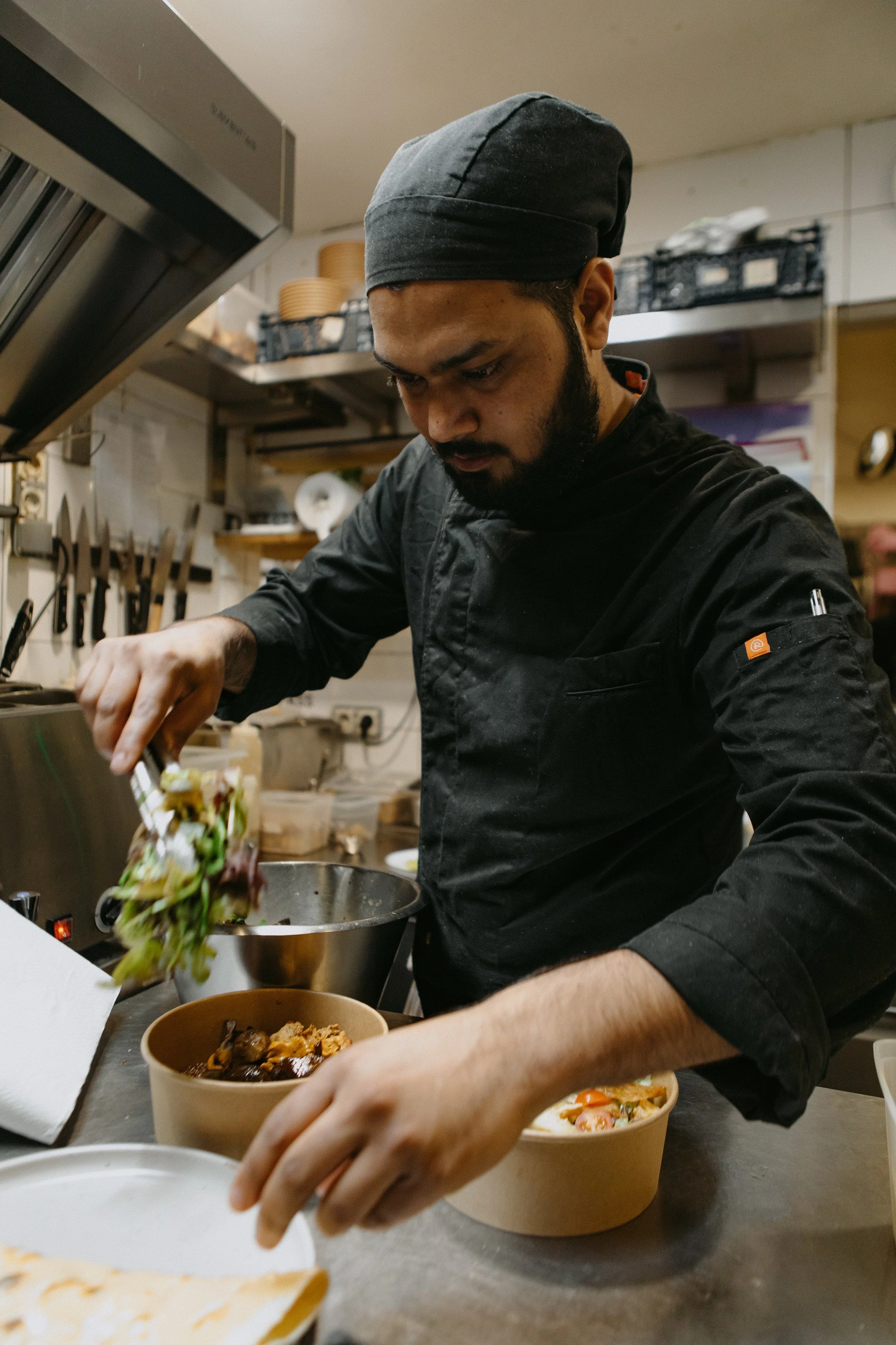 Un chef en tenue noire préparant des plats dans une cuisine professionnelle.