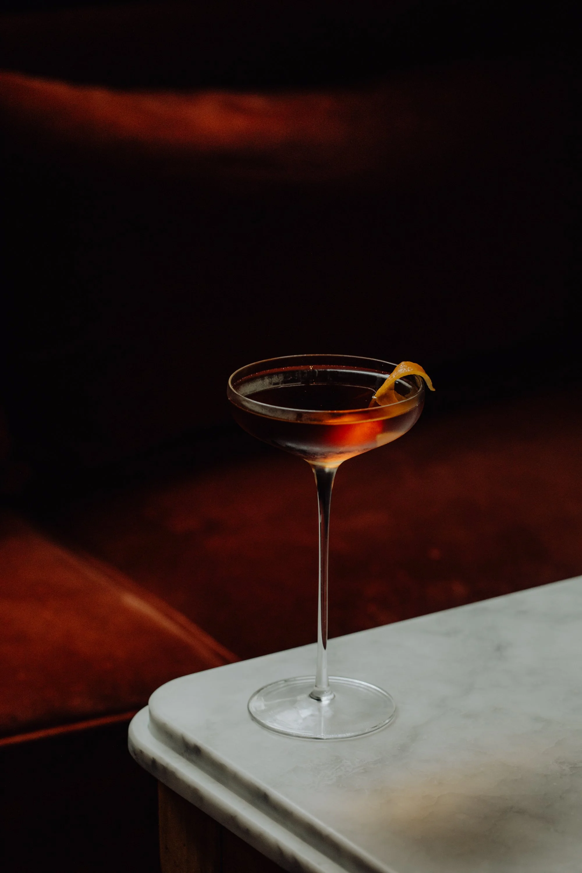 Un verre à cocktail avec un citron en décoration, placé sur une surface en marbre, fond sombre.