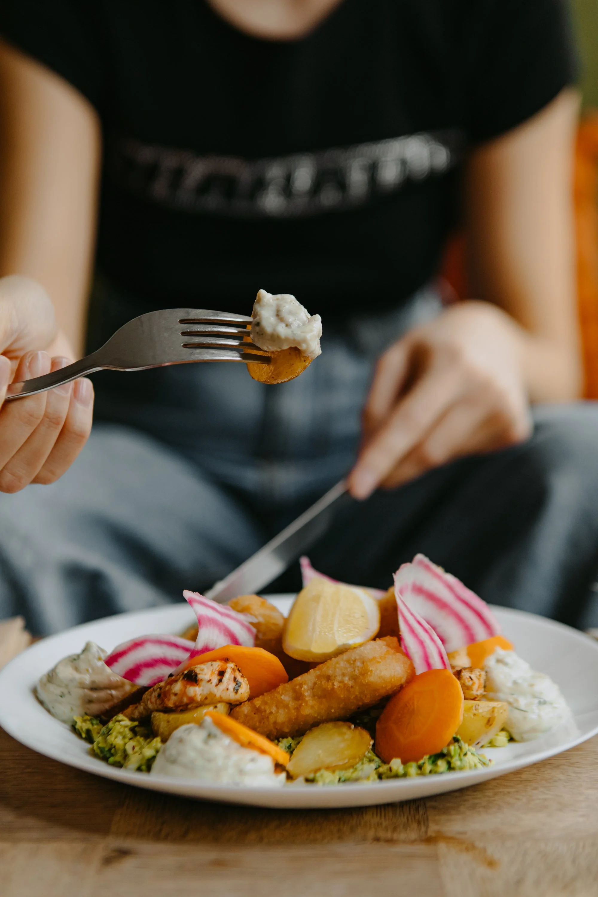 Person tenant un utinsile avec une portion de nourriture, avec un plateau rempli de légumes et de divers aliments dans un restaurant ou une maison.