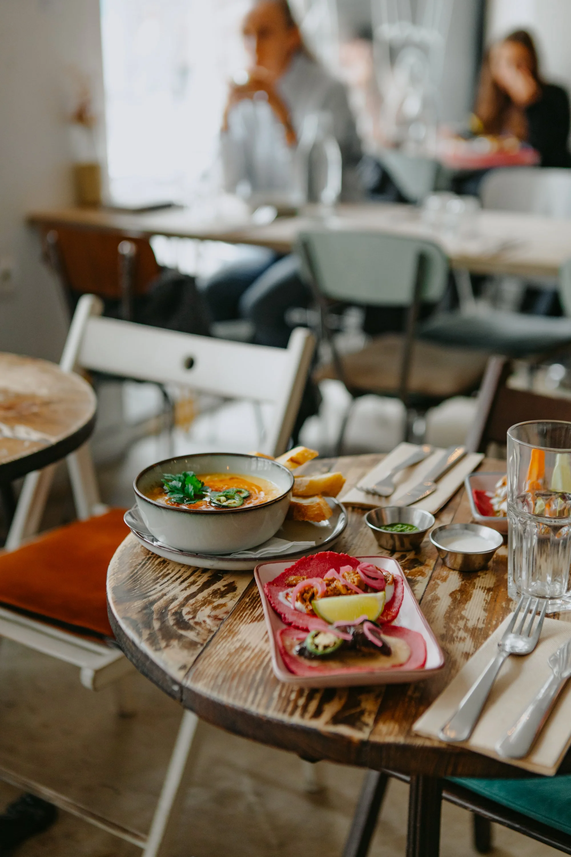 Repas de soupe et tacos mexicains sur une table en bois dans un restaurant. En arrière-plan, des personnes assises et discutant.