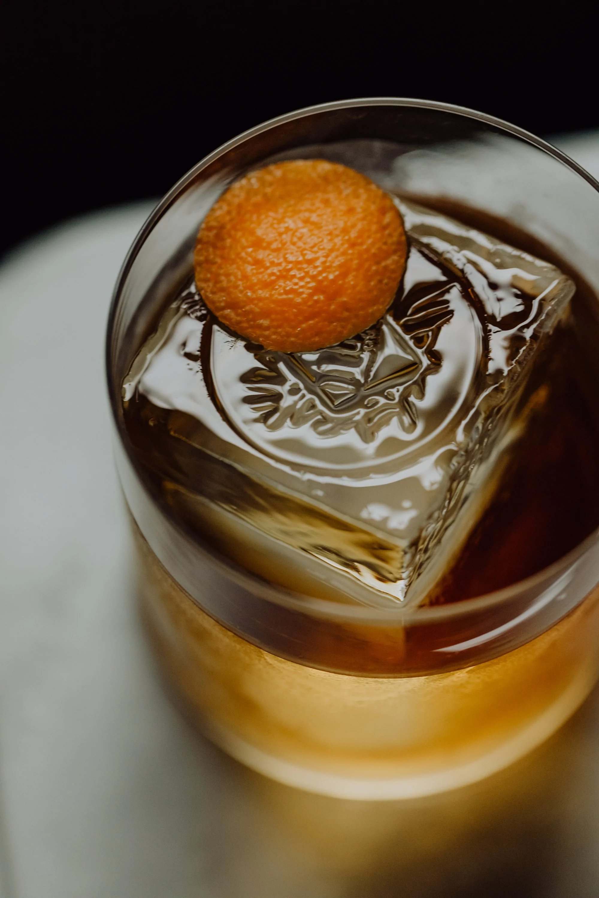 Verre de cocktail avec un glaçon en forme de carré et un zeste d'orange en décoration.