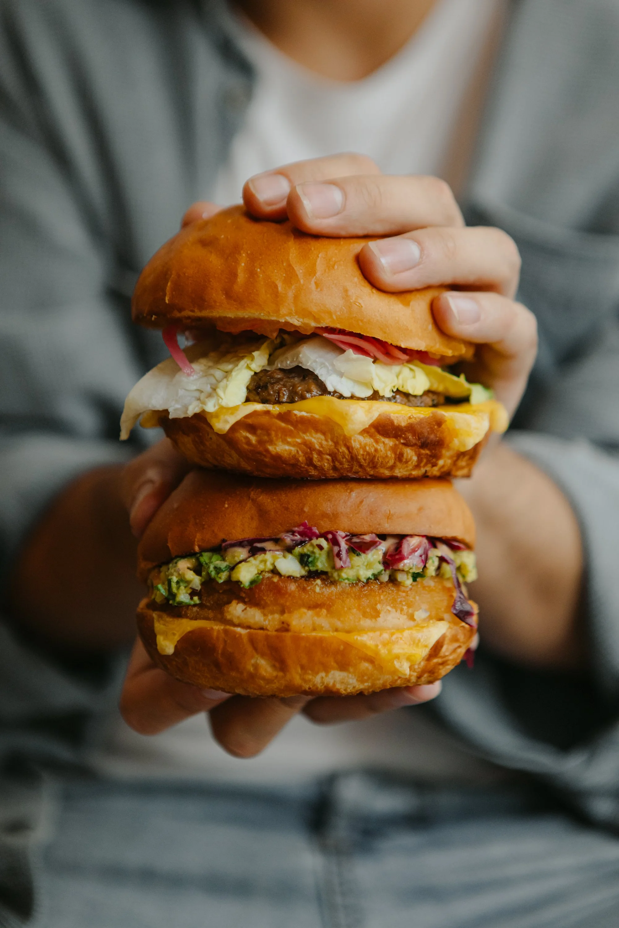 Une personne tient deux hamburgers empilés, avec différents ingrédients comme la viande, la salade et les tomates.