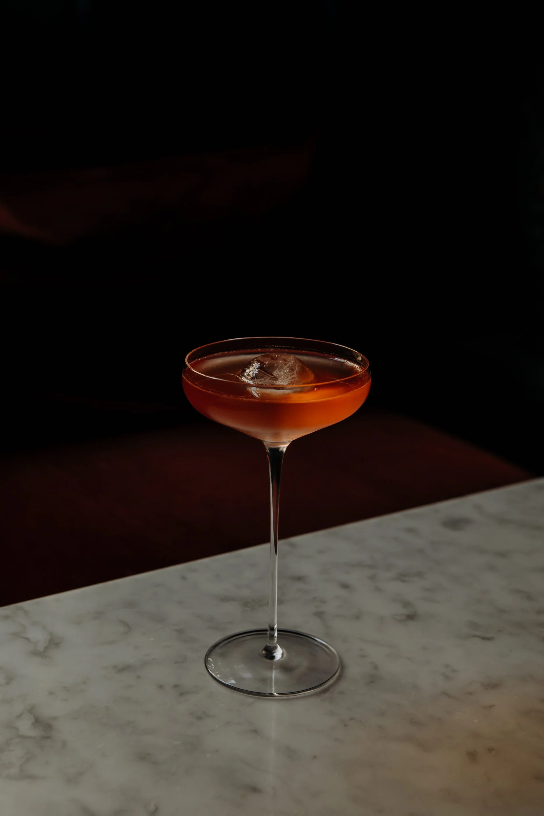 Cocktail orange dans un verre à cocktail sur une table en marbre noir, fond sombre.