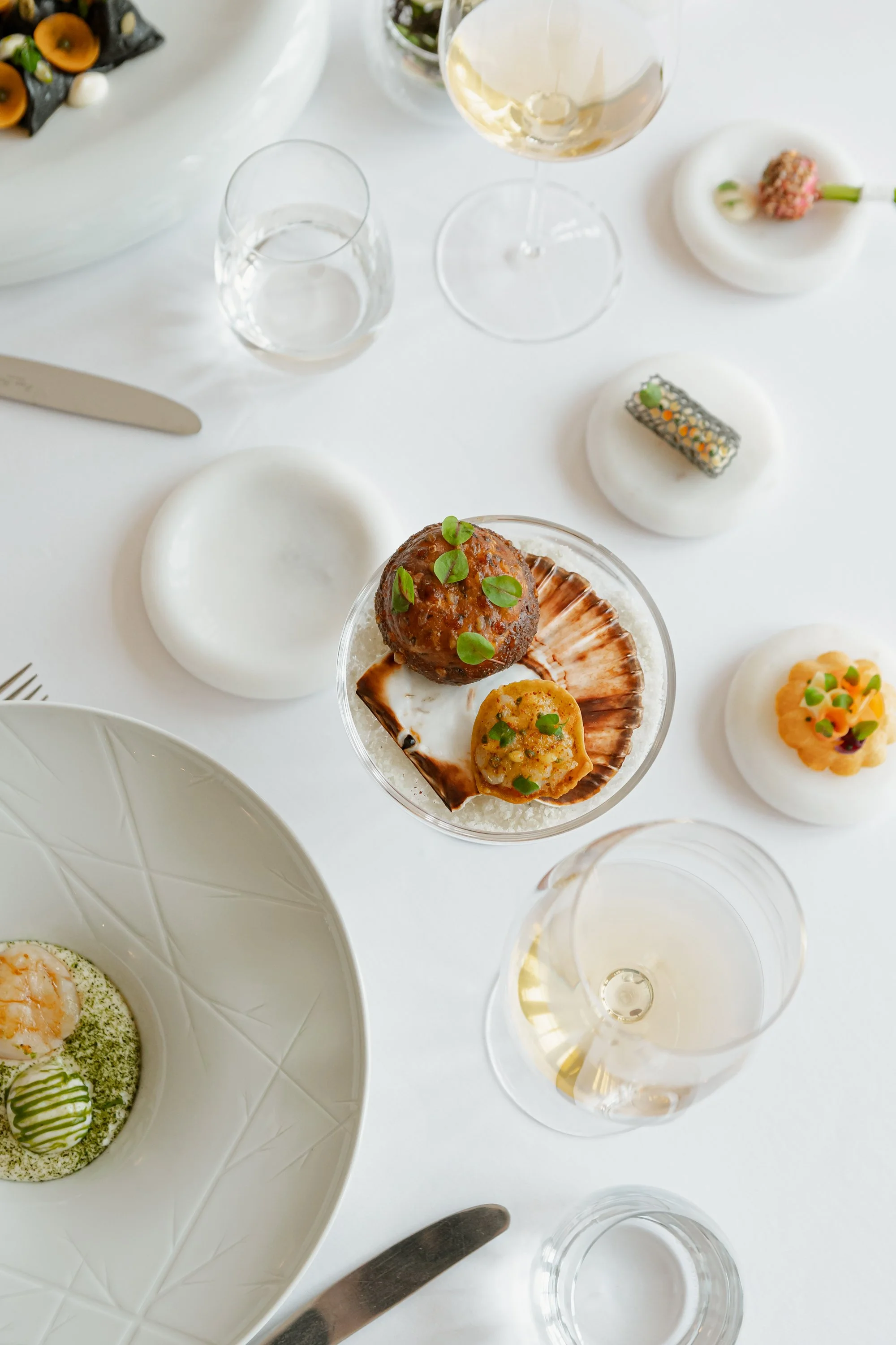 Assiette de amuse-bouches gastronomiques, verres de vin blanc, assiettes blanches, éléments de présentation sophistiqués, table élégante.
