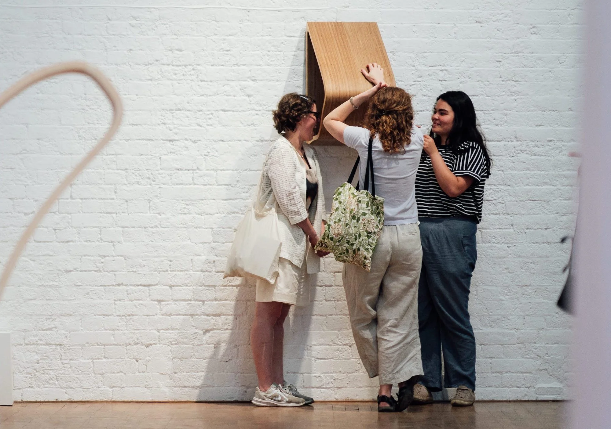 Three women standing in an art gallery, looking at a piece of artwork on the wall.