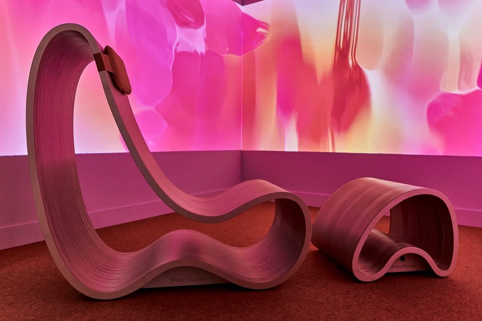 Curvy shaped lounger chair and footstool made of wood with a bright pink abstract background
