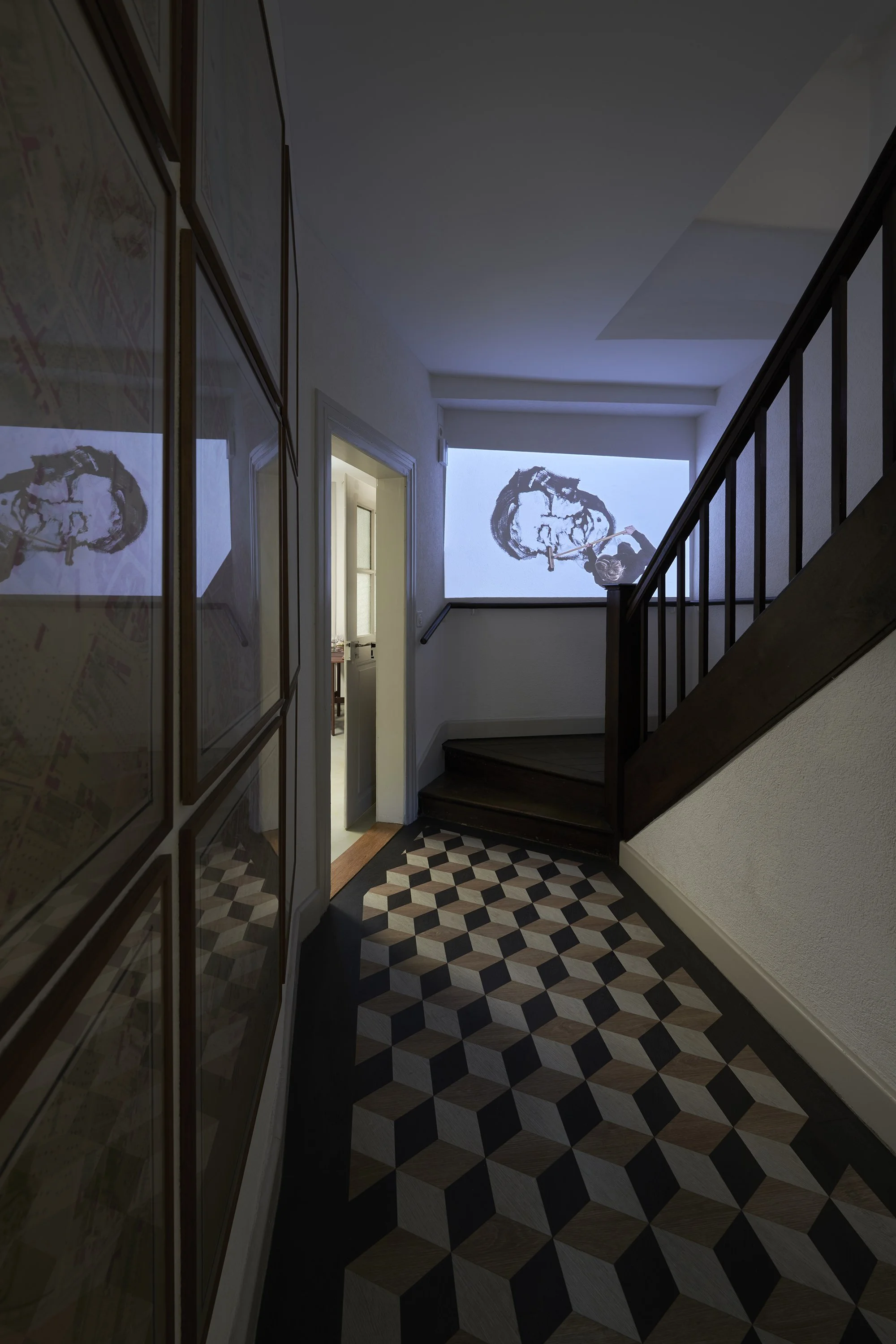 Installation view of a stairwell with a checkered floor and a video by Karoline Schreiber displayed near the entrance