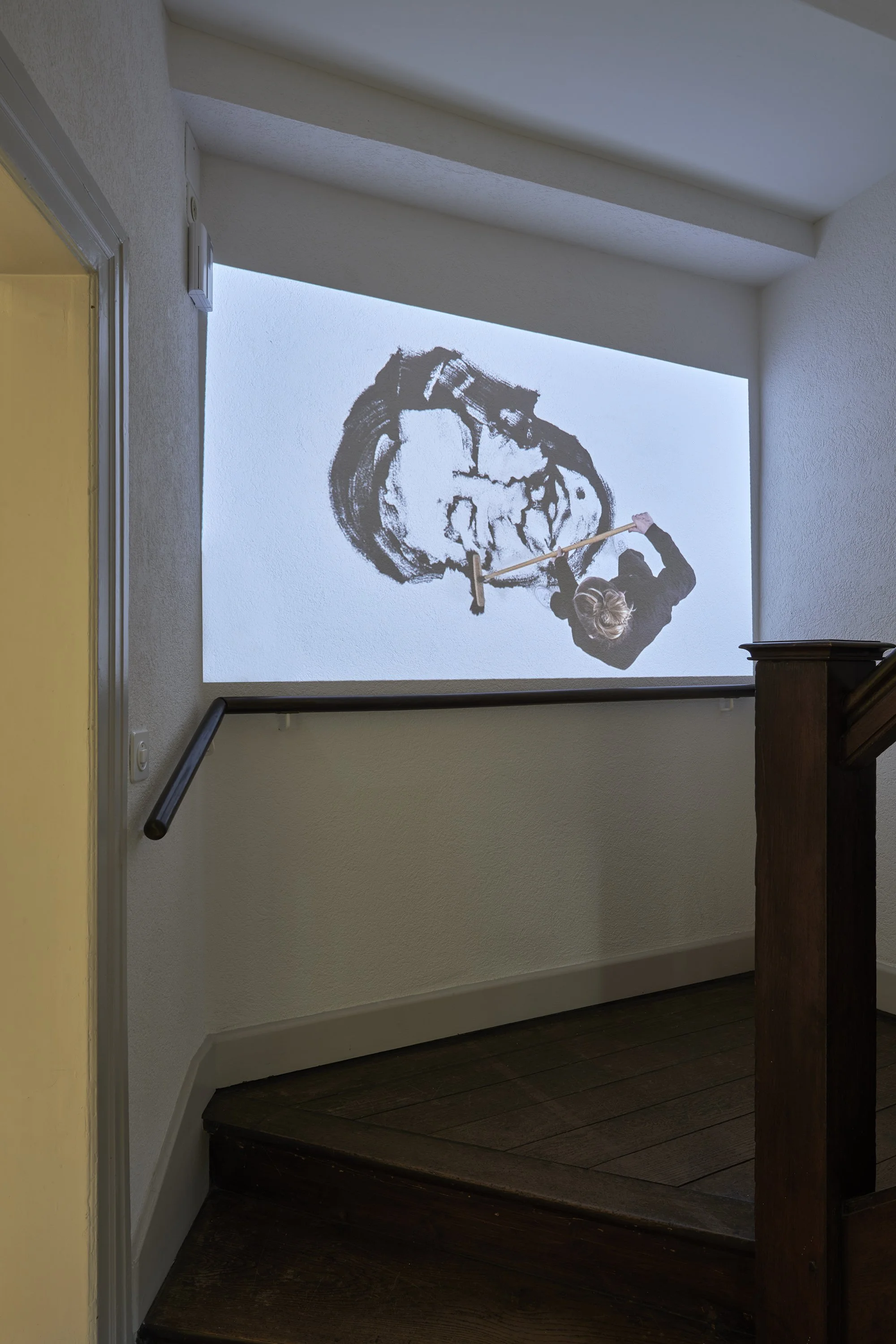 Installation view of a large figurative video performance by Karoline Schreiber displayed above a staircase landing