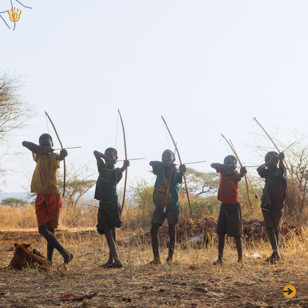 A front view picture showing a Hadzabe kids in a line holding their bow and arrows