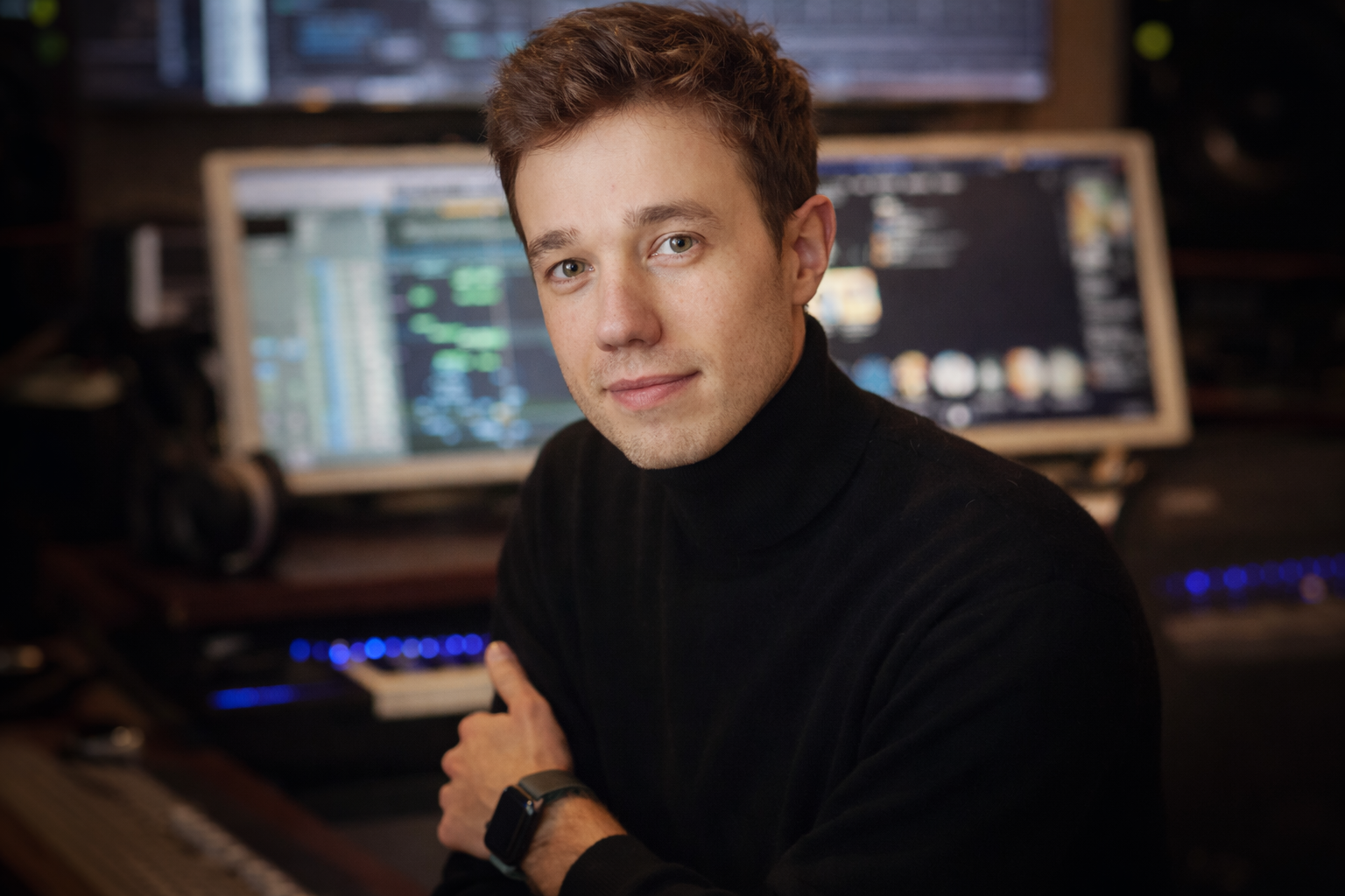 Un homme en pulled noir devant un écran d'ordinateur avec un logiciel de musique ou de montage vidéo.