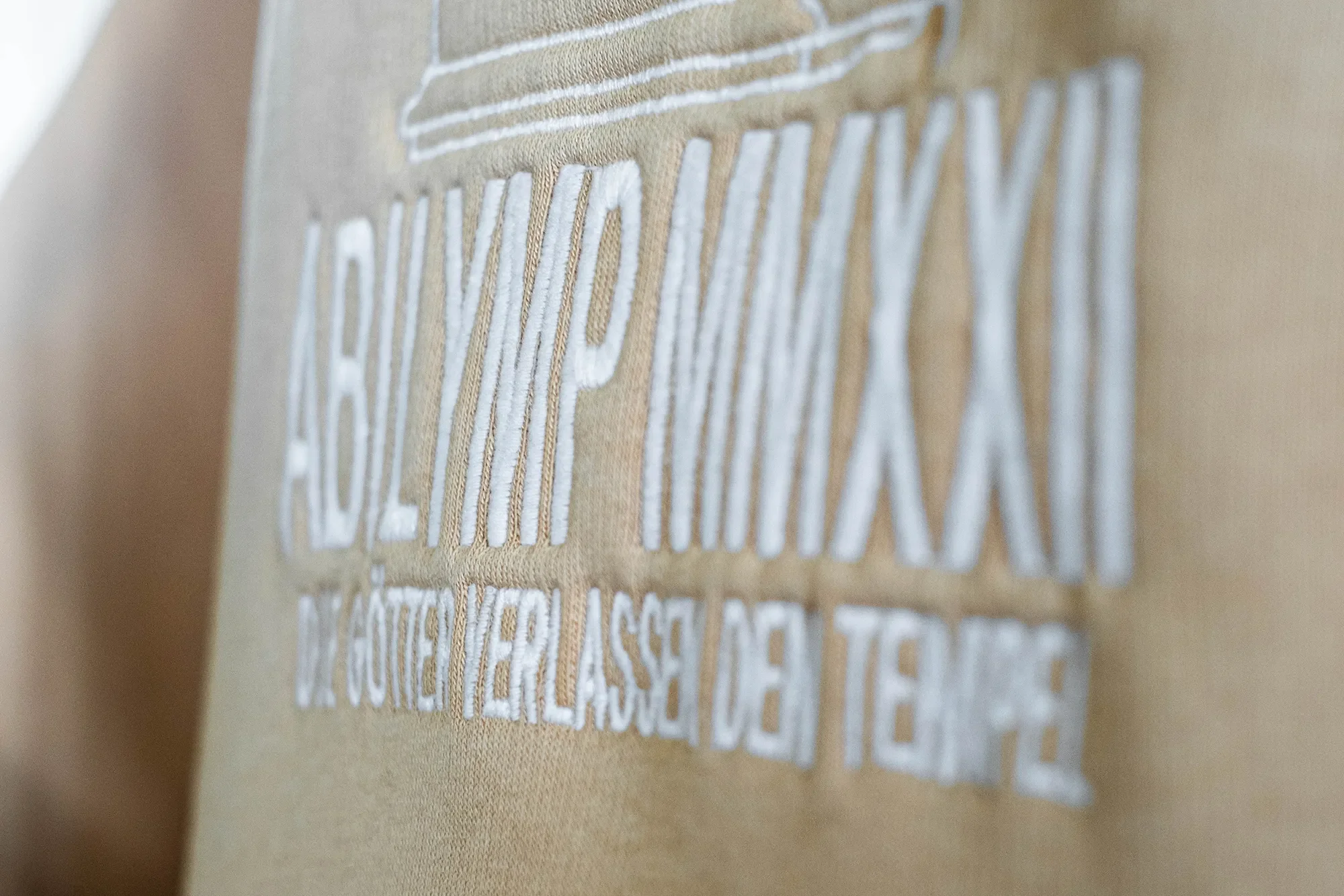 Nahaufnahme eines beige Stoffes mit weißen Stickbuchstaben, die zum Teil lesbar sind.