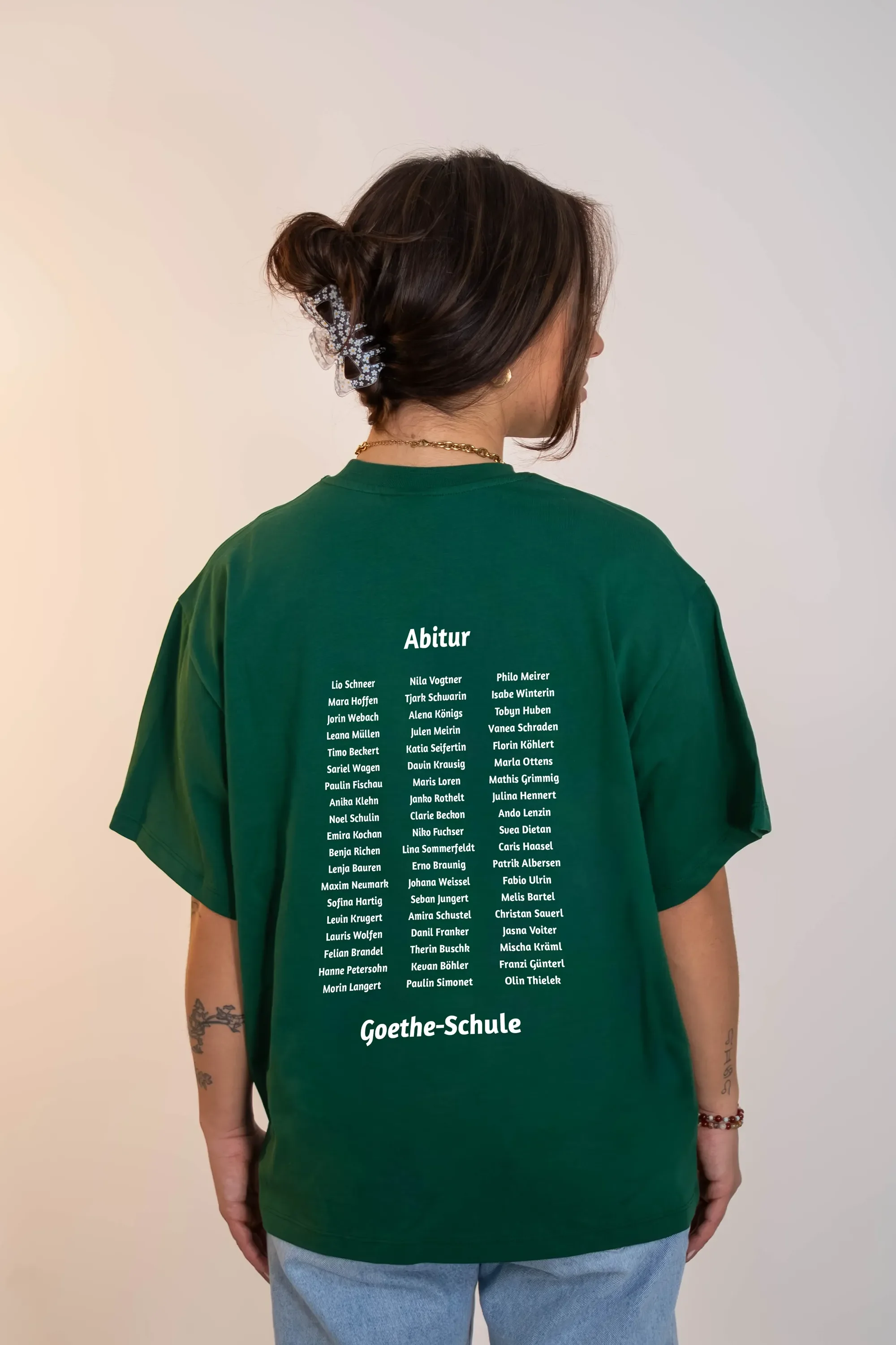 Eine Person trägt ein grünes T-Shirt mit einer Liste von Namen und der Aufschrift 'Abitur' und 'Goethe-Schule' auf der Rückseite.