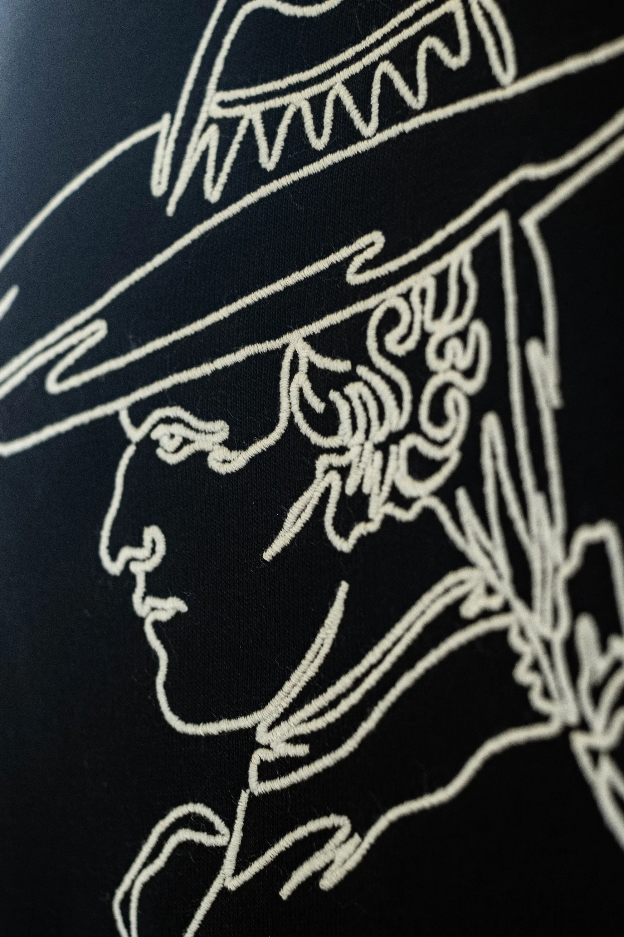Nahaufnahme eines schwarzen Stoffes mit weißem Stickmuster eines Künstlers, der einen Hut trägt.