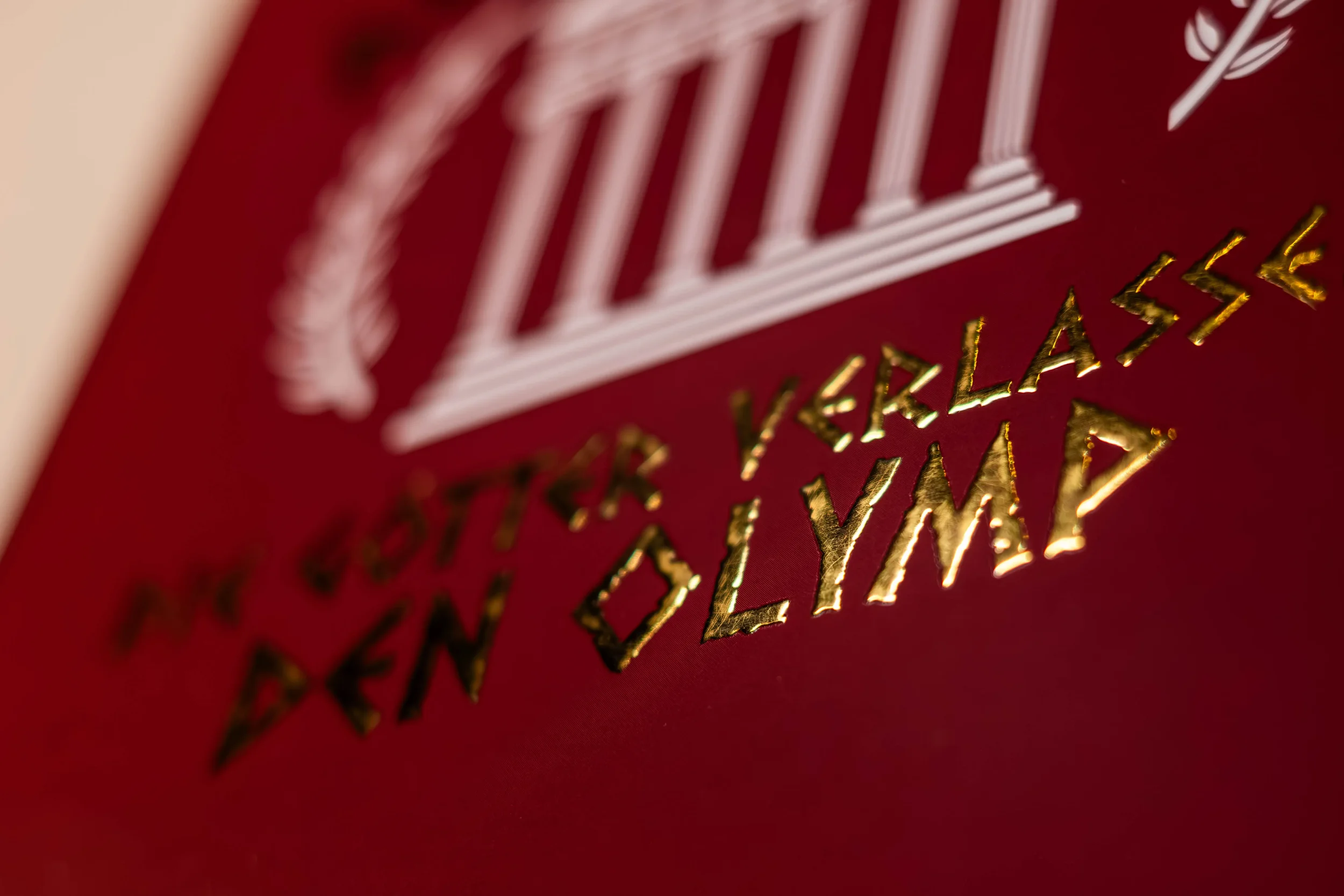 Nahaufnahme eines roten Helms mit goldenem Text 'Paritter Verklaße Den Olymp' und weißen Säulen im Design.