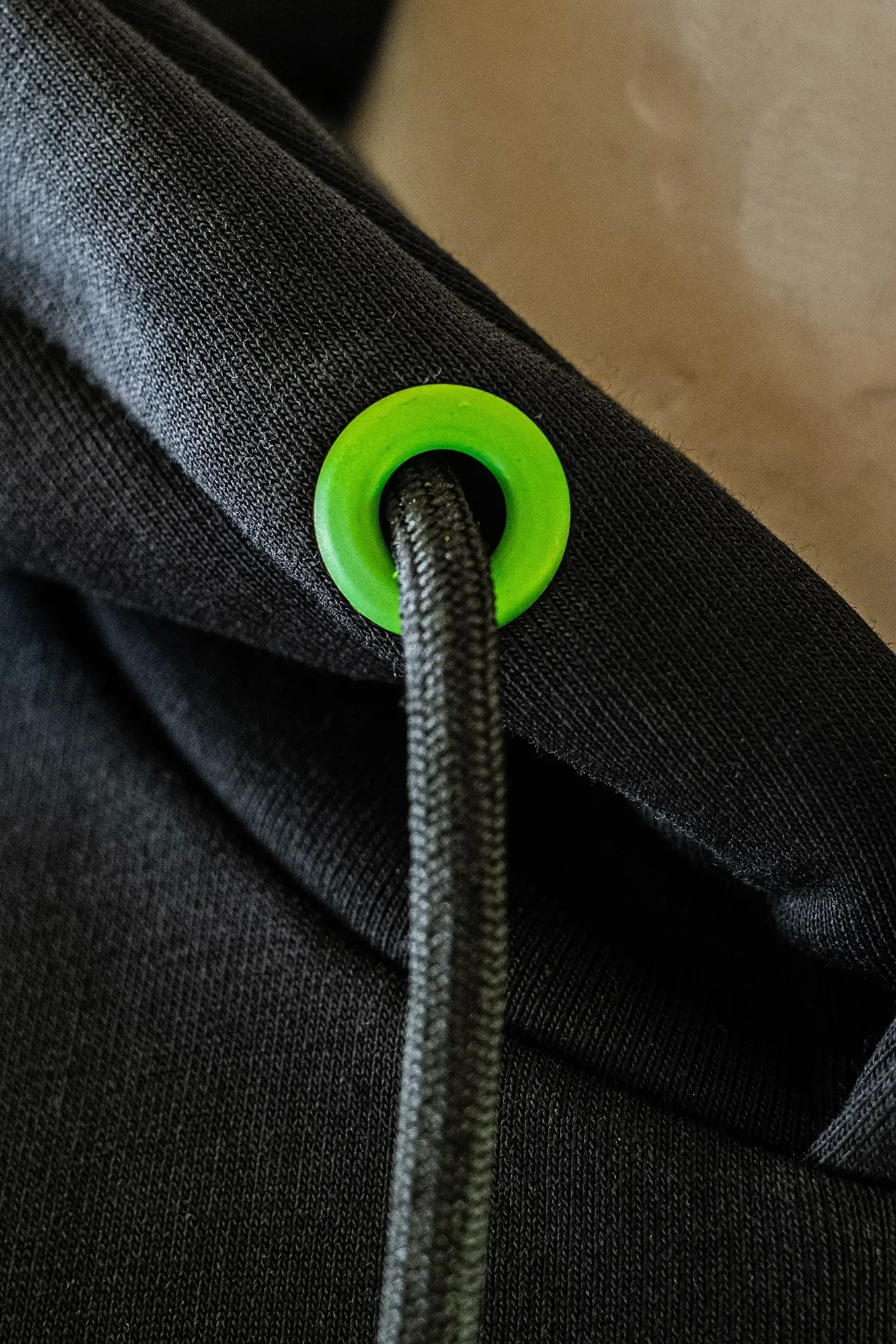 Nahaufnahme eines schwarzen Kleidungsstücks mit einer grünen Öse und einem schwarzen Kordelzug.
