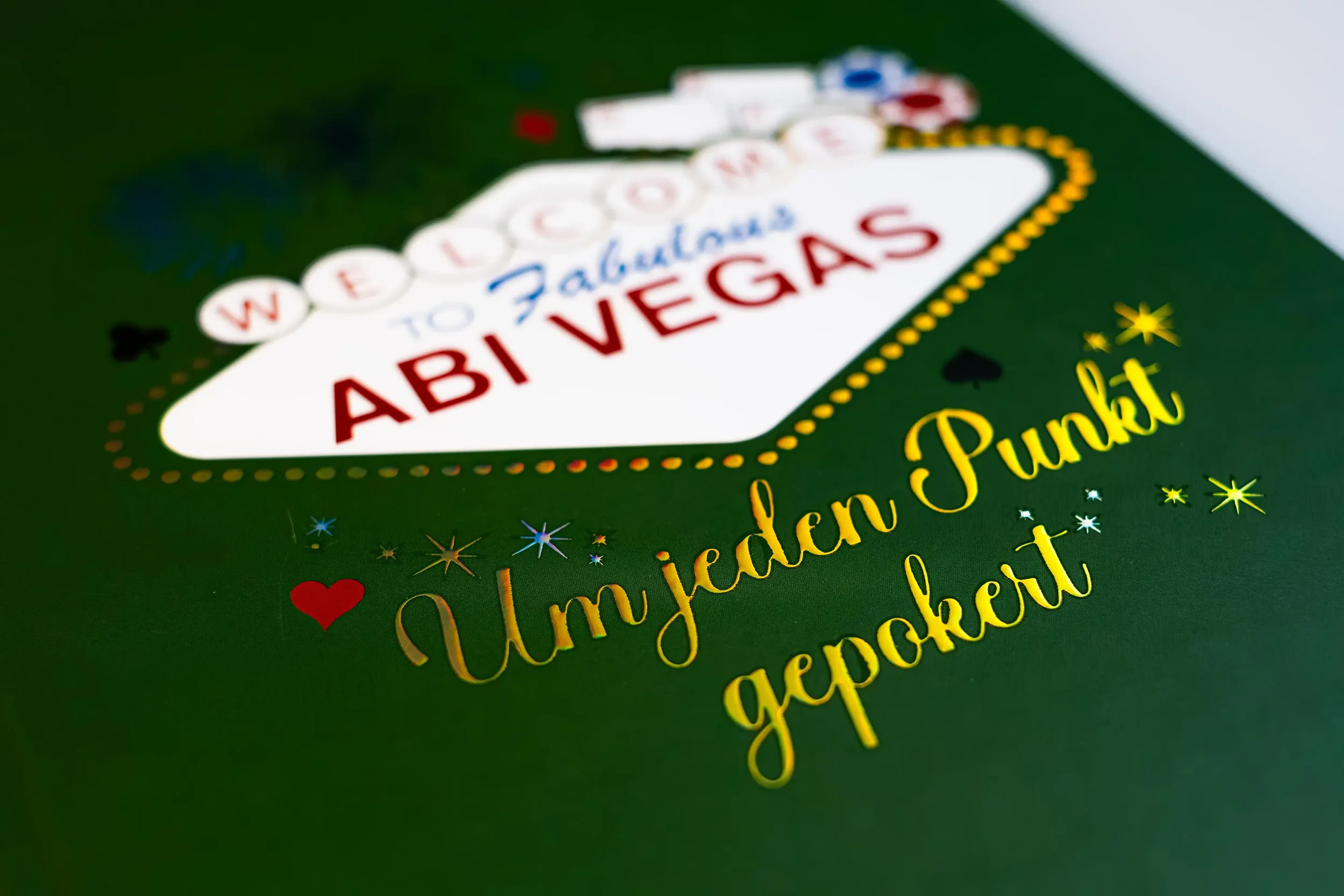 Eine grüne Oberseite einer Spielkarte mit dem Schriftzug "Willkommen zu Fabulous AB! VEGAS" und der Nachricht "Um was für ein Punkter gespielt" in goldener Schrift, mit kleinen dekorativen Sternen und Herzen.