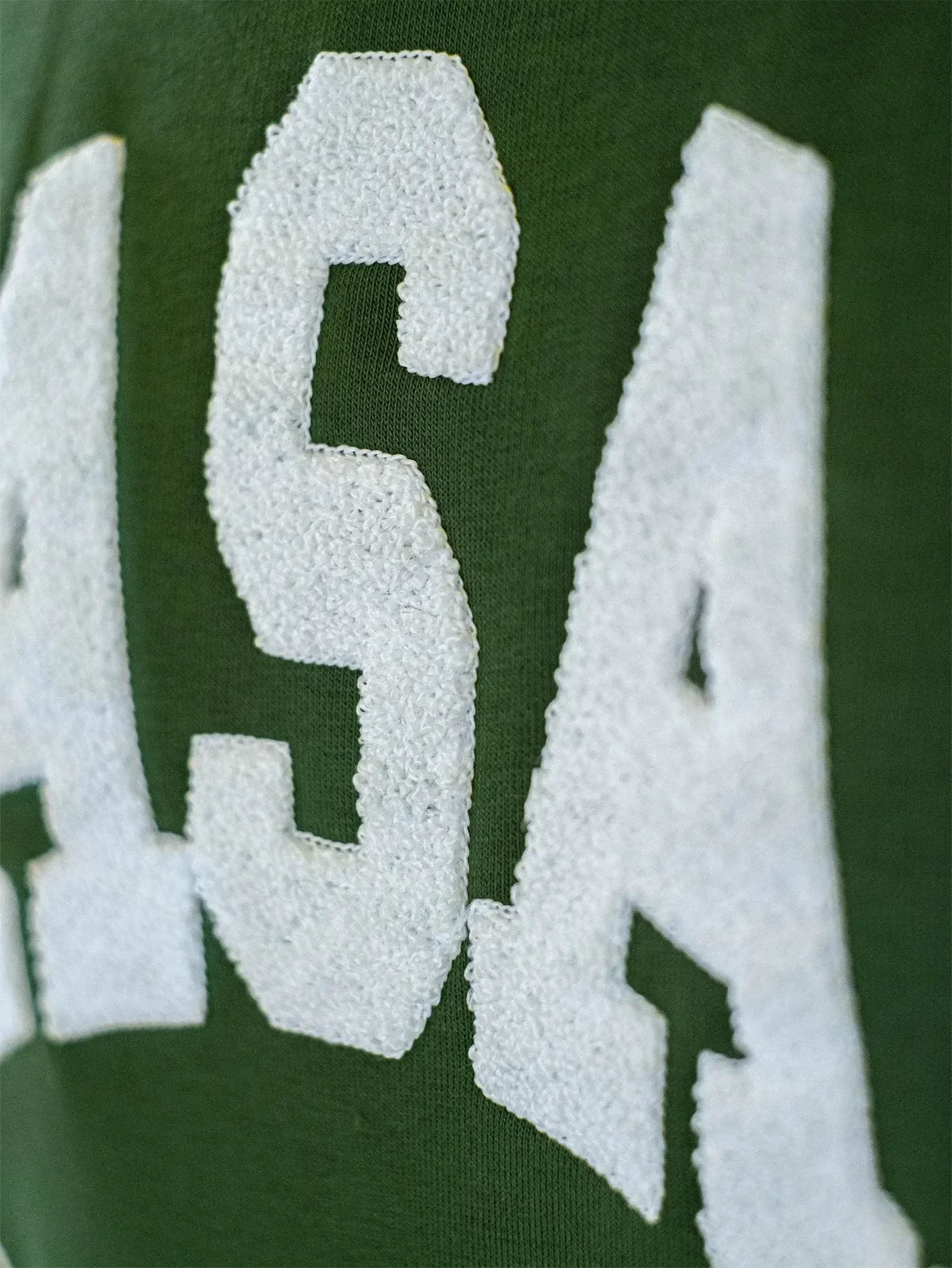 Nahaufnahme eines grünen Stoffes mit weißen, aufgestickten Buchstaben.