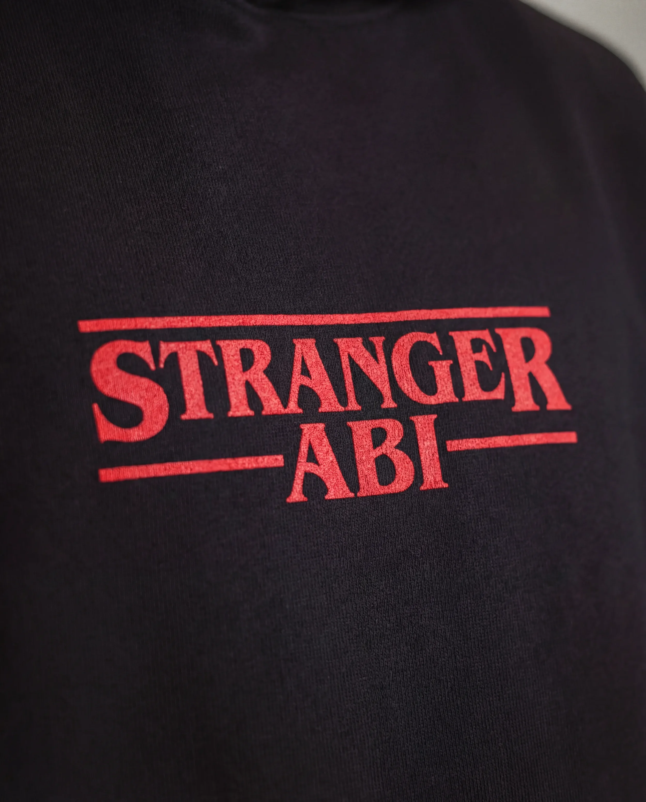 Nahaufnahme eines schwarzen T-Shirts mit rotem Aufdruck, der den Text "STRANGER ABLE" enthält.