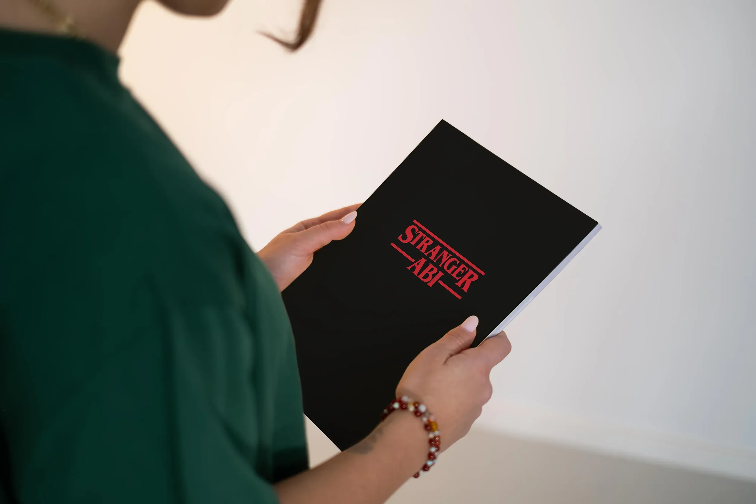 Eine Person hält ein schwarzes Buch mit dem Titel "Stranger Abi" in roter Schrift gegen weißen Hintergrund.