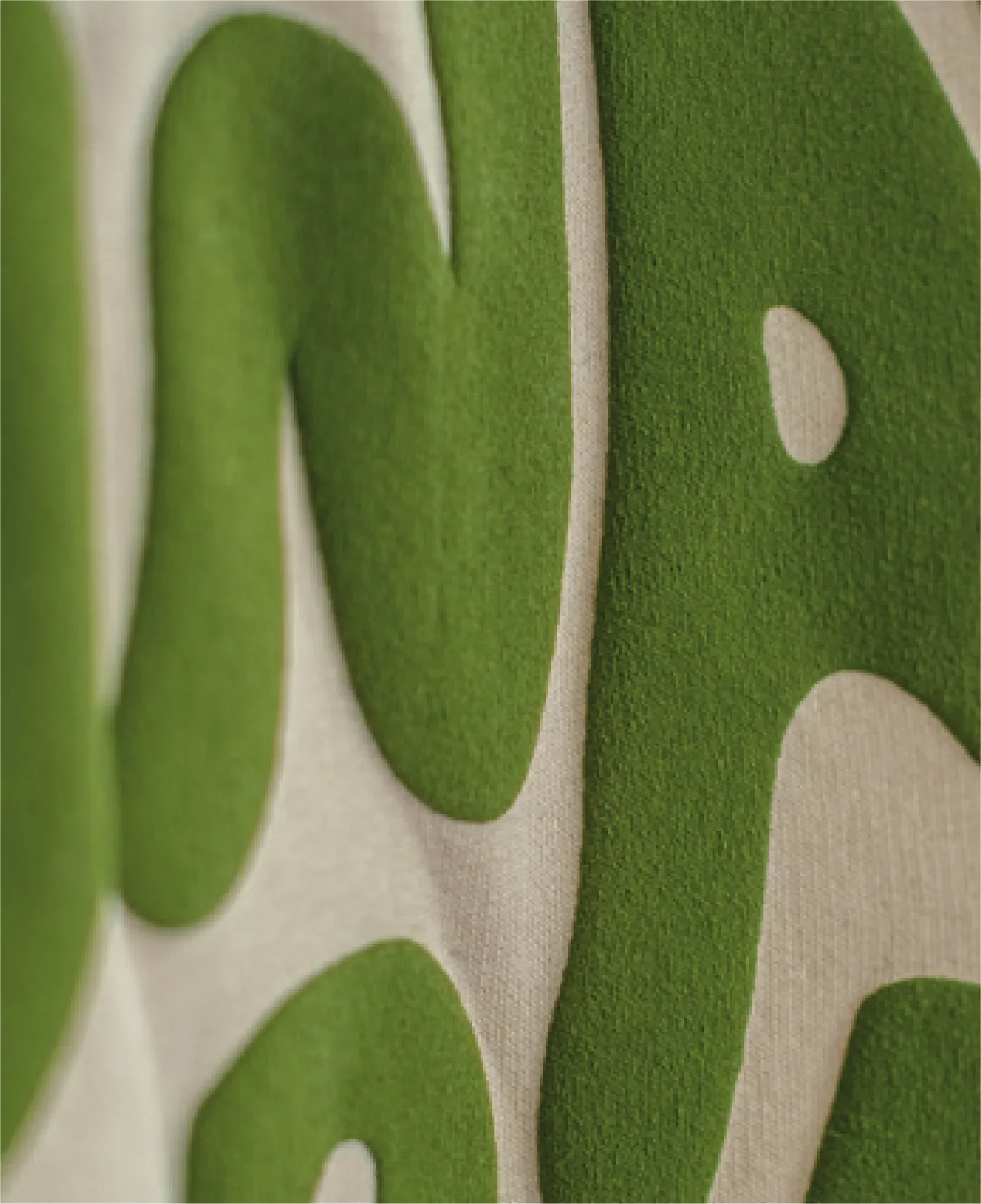 Nahaufnahme eines grünen, mehrschichtigen Stoffbuchstabens auf beigem Hintergrund.