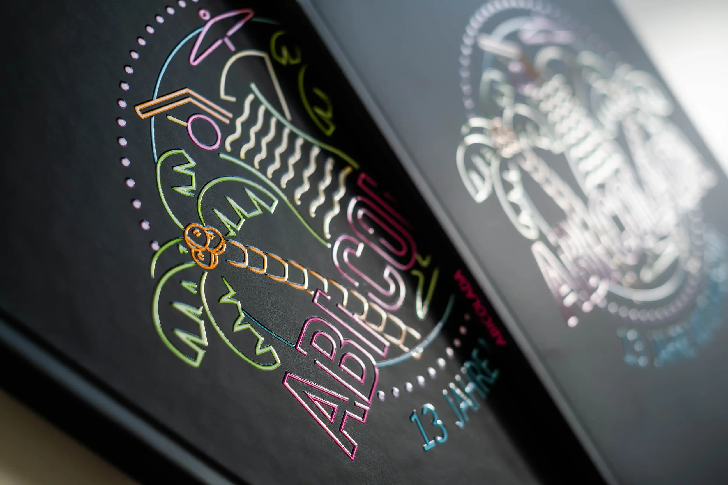 Ausgelaserte, bunte Text- und Bildgestaltung auf einer schwarzen Oberfläche, mit der Aufschrift 'Absolut 13 Jahre'.