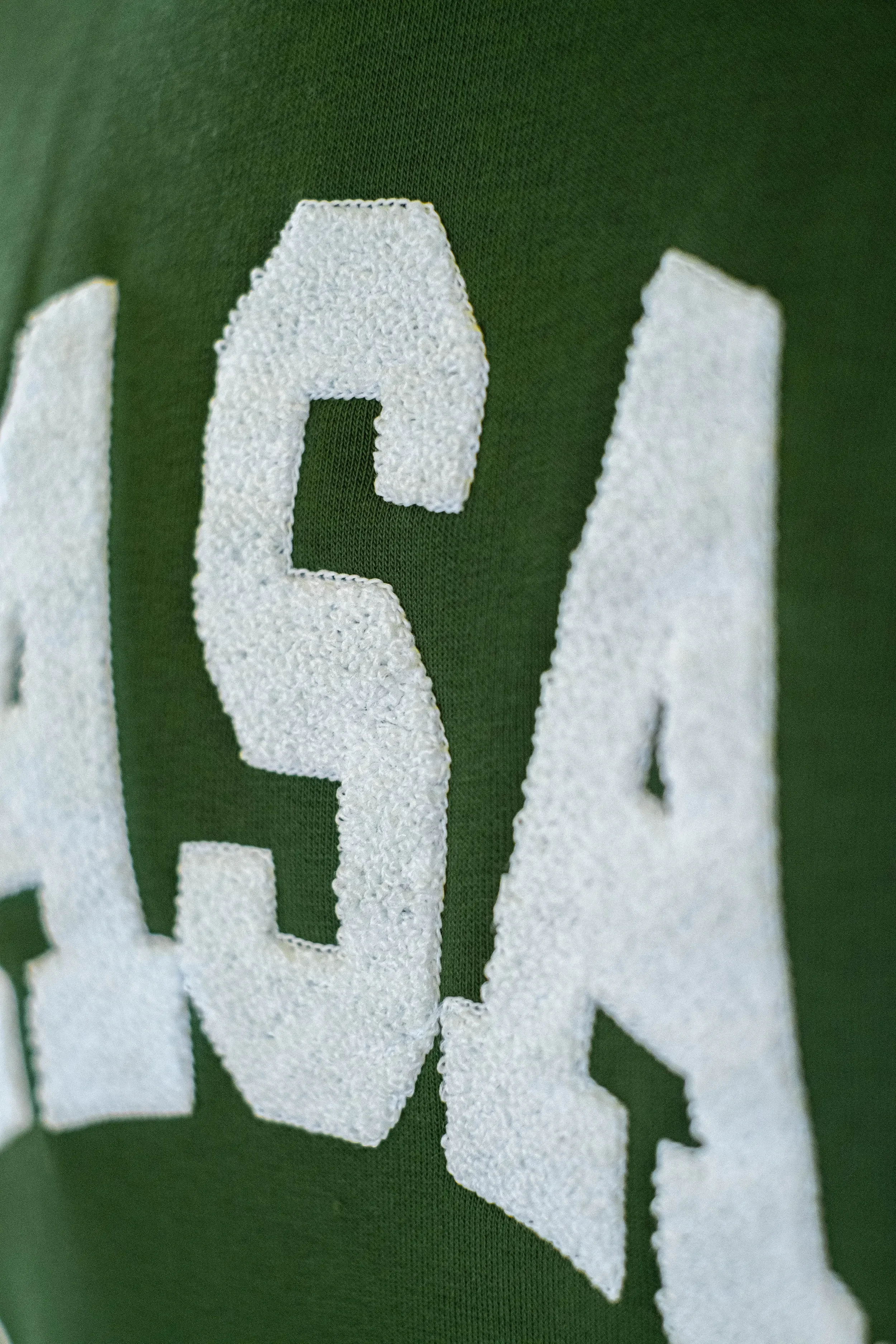 Nahaufnahme eines grünen Stoffes mit weißen, aufgewebten Buchstaben.