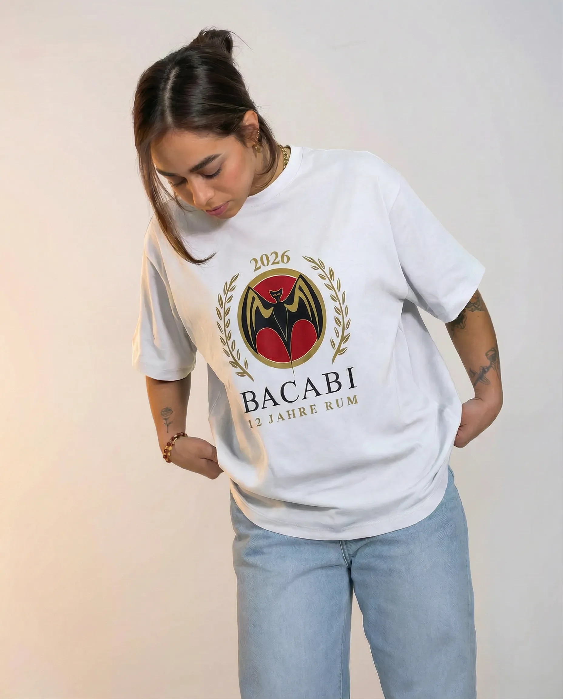 Junge Frau trägt weißen T-Shirt mit Bacardi-Logo, der Text "2026 12 Jahre Rum" zeigt, steht vor weißem Hintergrund.