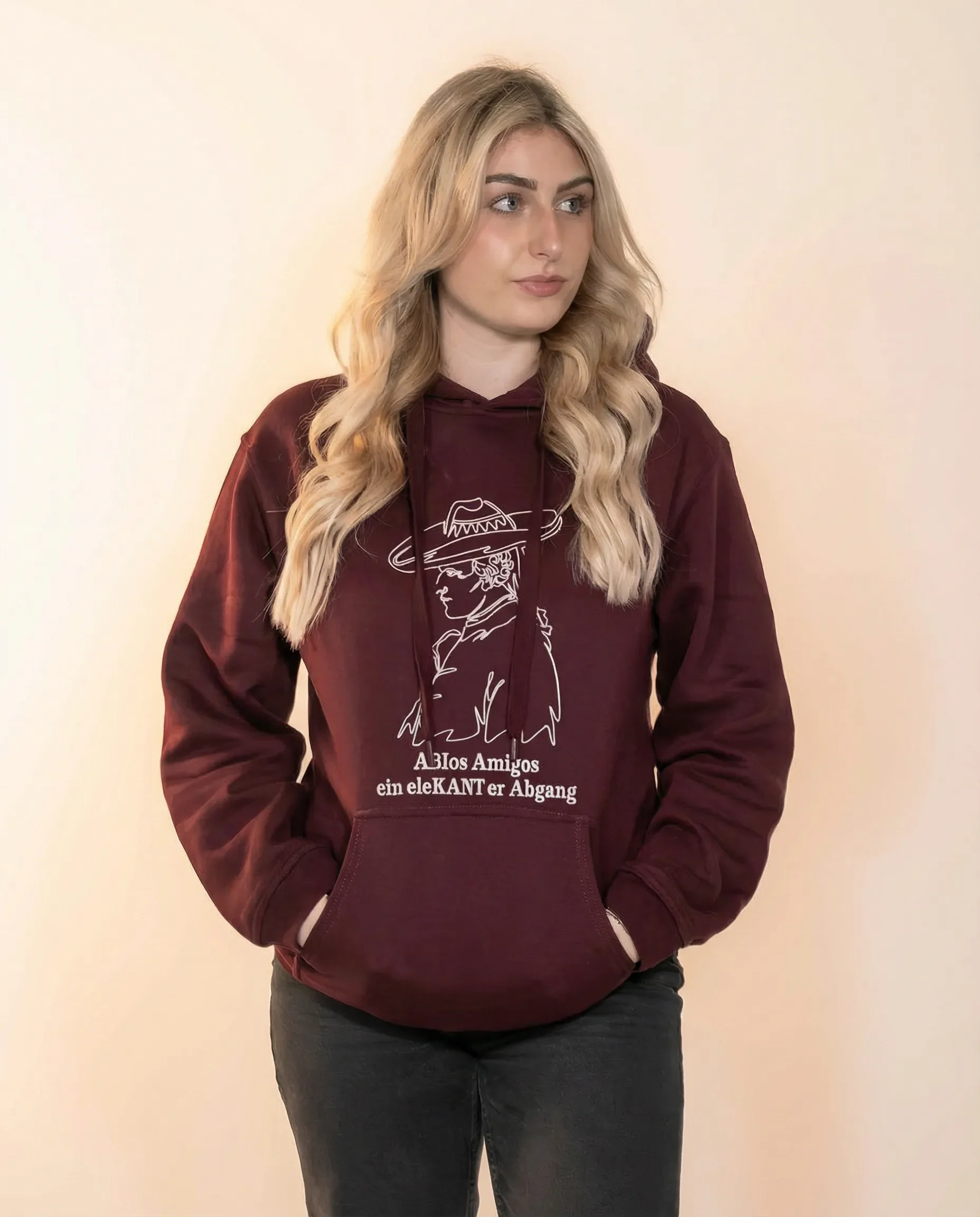 Junge Frau trägt einen dunkelroten Hoodie mit weißen Linienzeichnung und Text in einer neutralen, hellen Umgebung.