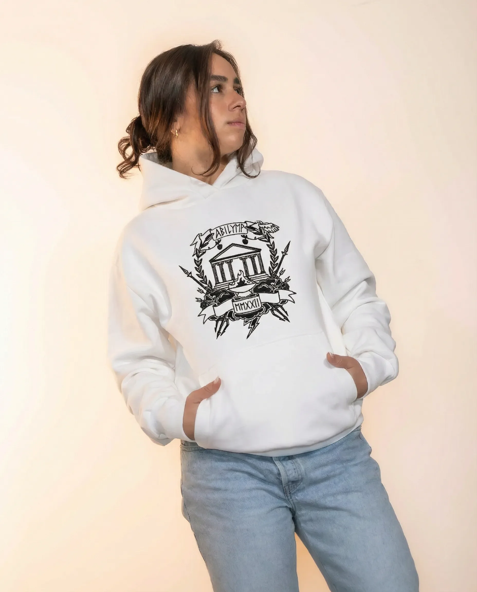 Frau trägt weißen Hoodie mit schwarz-weißem Design, das eine antike griechische Tempelanlage, Laubkränze, Blitze und römische Zahlen zeigt.