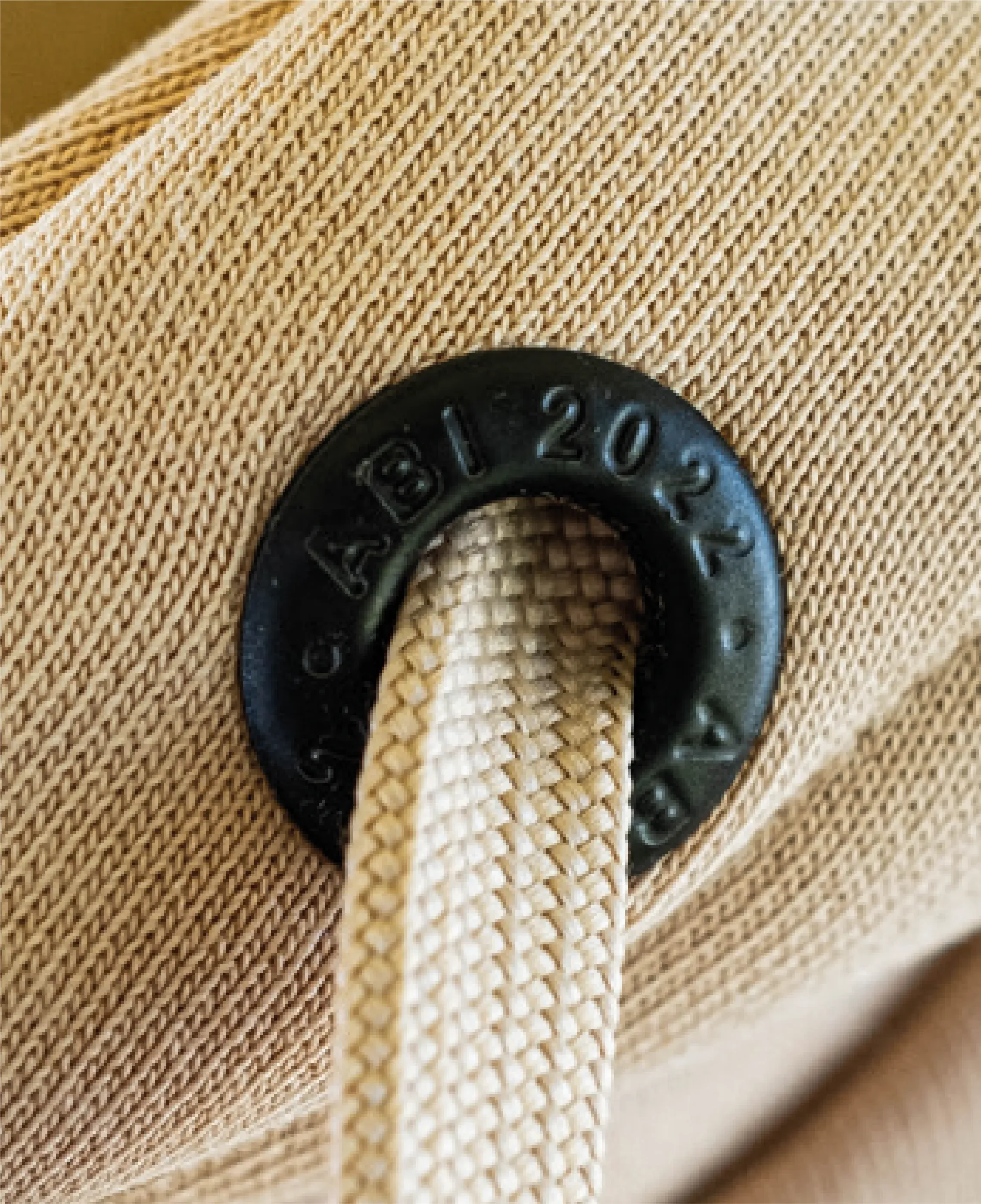 Nahaufnahme eines beige Canvasrucksacks mit schwarzen Metallringen und einem gezackten Riemen.