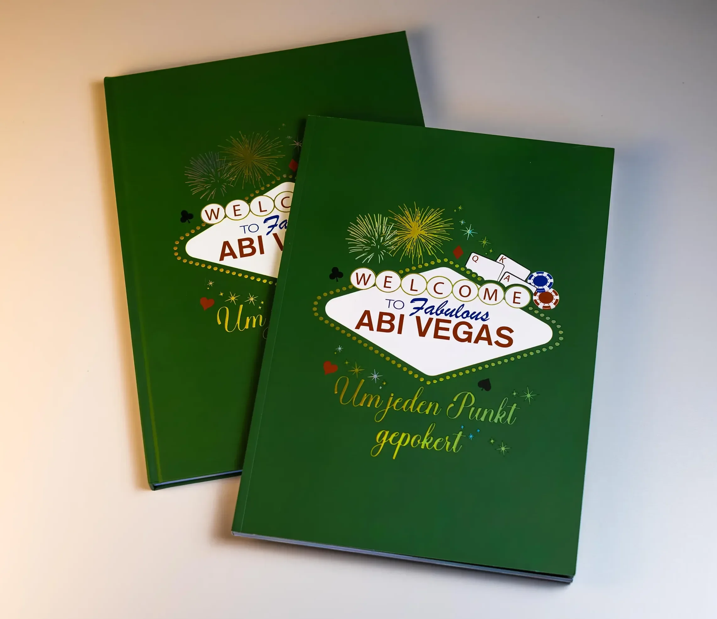 Zwei grüne Buchcover mit einem Willkommensgruß für eine Reise nach Vegas, verziert mit Feuerwerksbildern, Spielkarten, Pokerchips, Herzen, Pik, Karo, Kreuz und Glitzer.