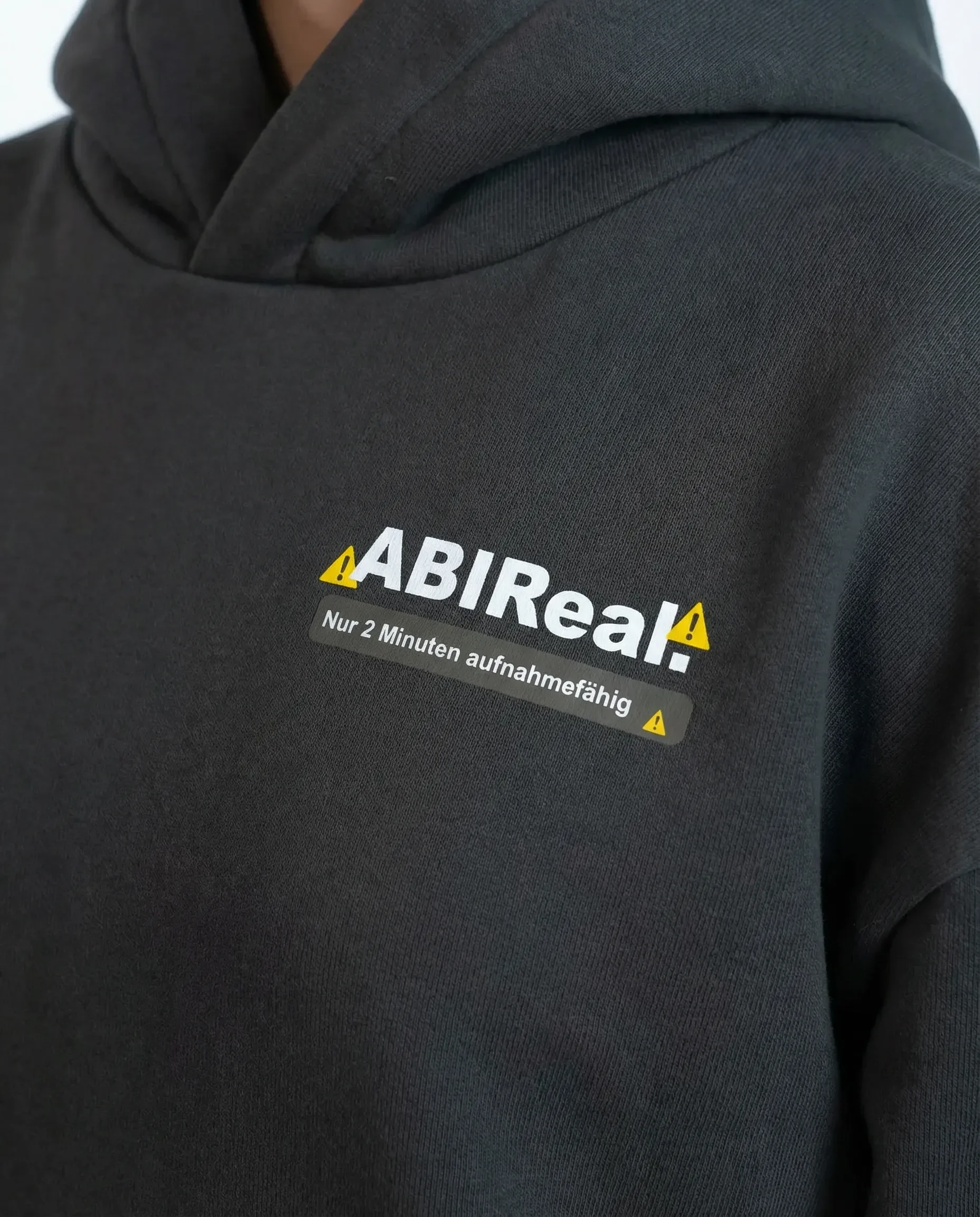 Schwarzer Pullover mit Aufdruck 'ABIRéal: Nur 2 Minuten aufnahmefähig' mit Warnsymbolen.