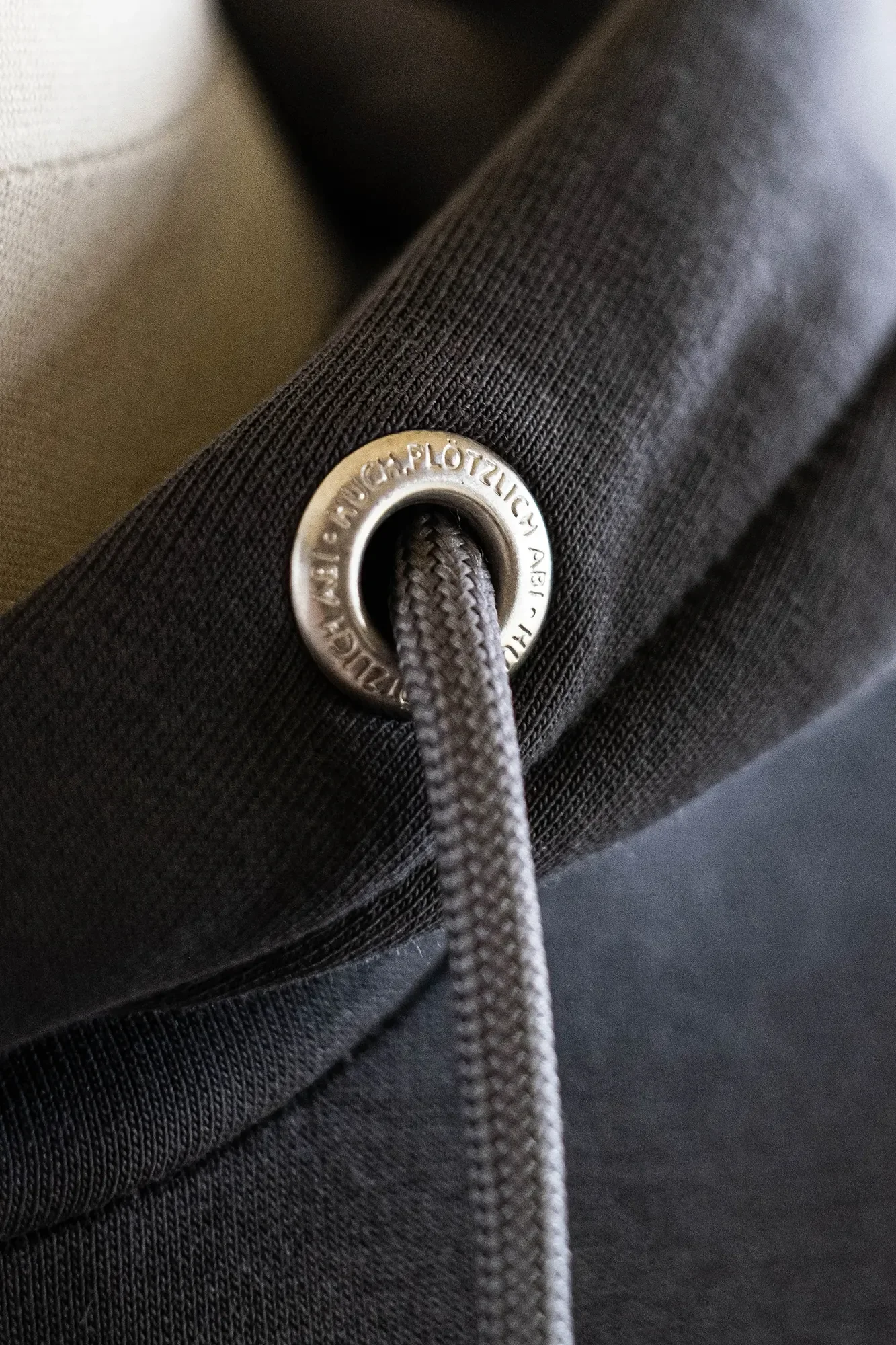 Nahaufnahme eines schwarzen Textilstücks mit Metallösen und grauem Schnürsenkel.