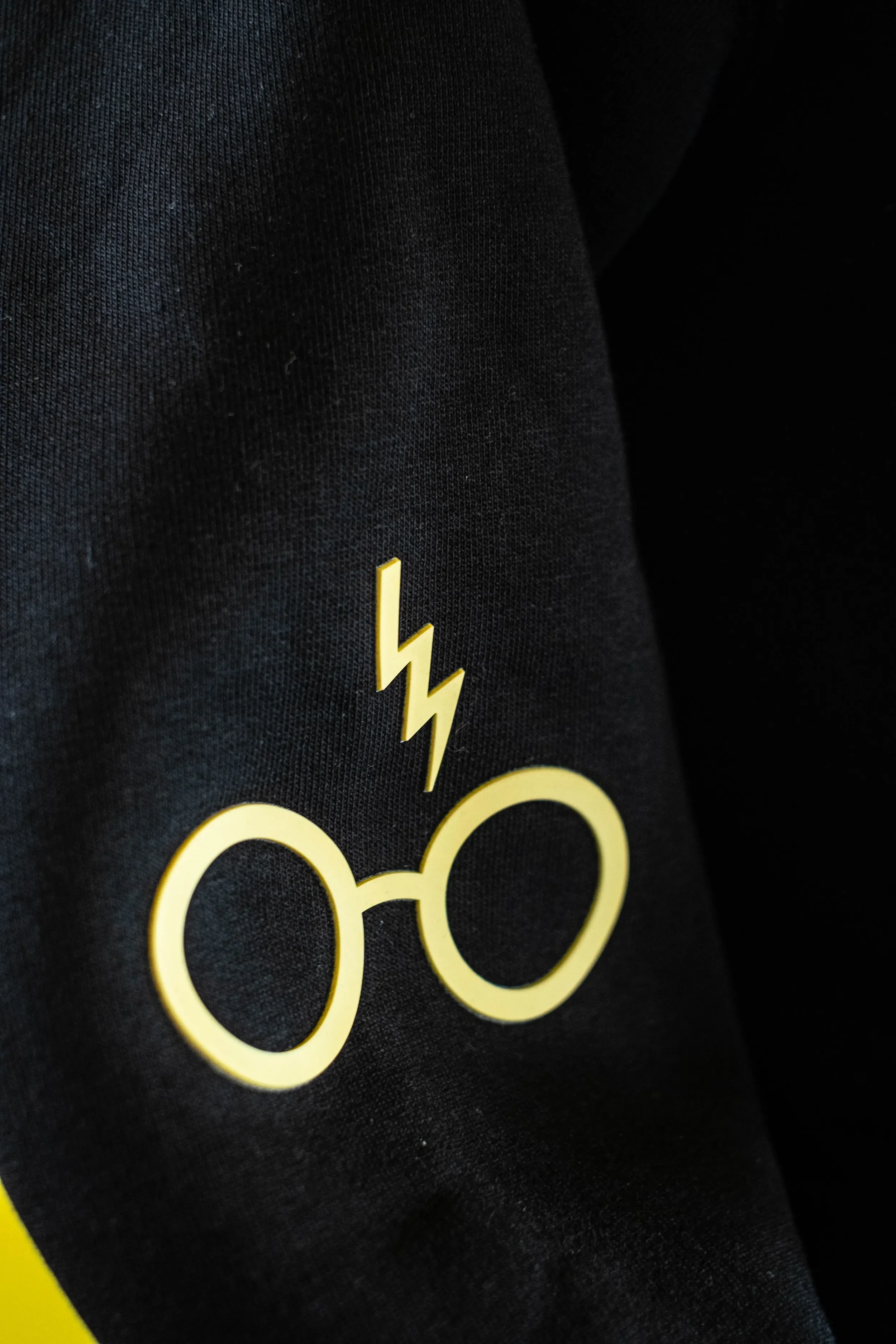 Nahaufnahme eines schwarzen Kleidungsstücks mit gelbem Druck, der eine Brille und einen Blitz zeigt.