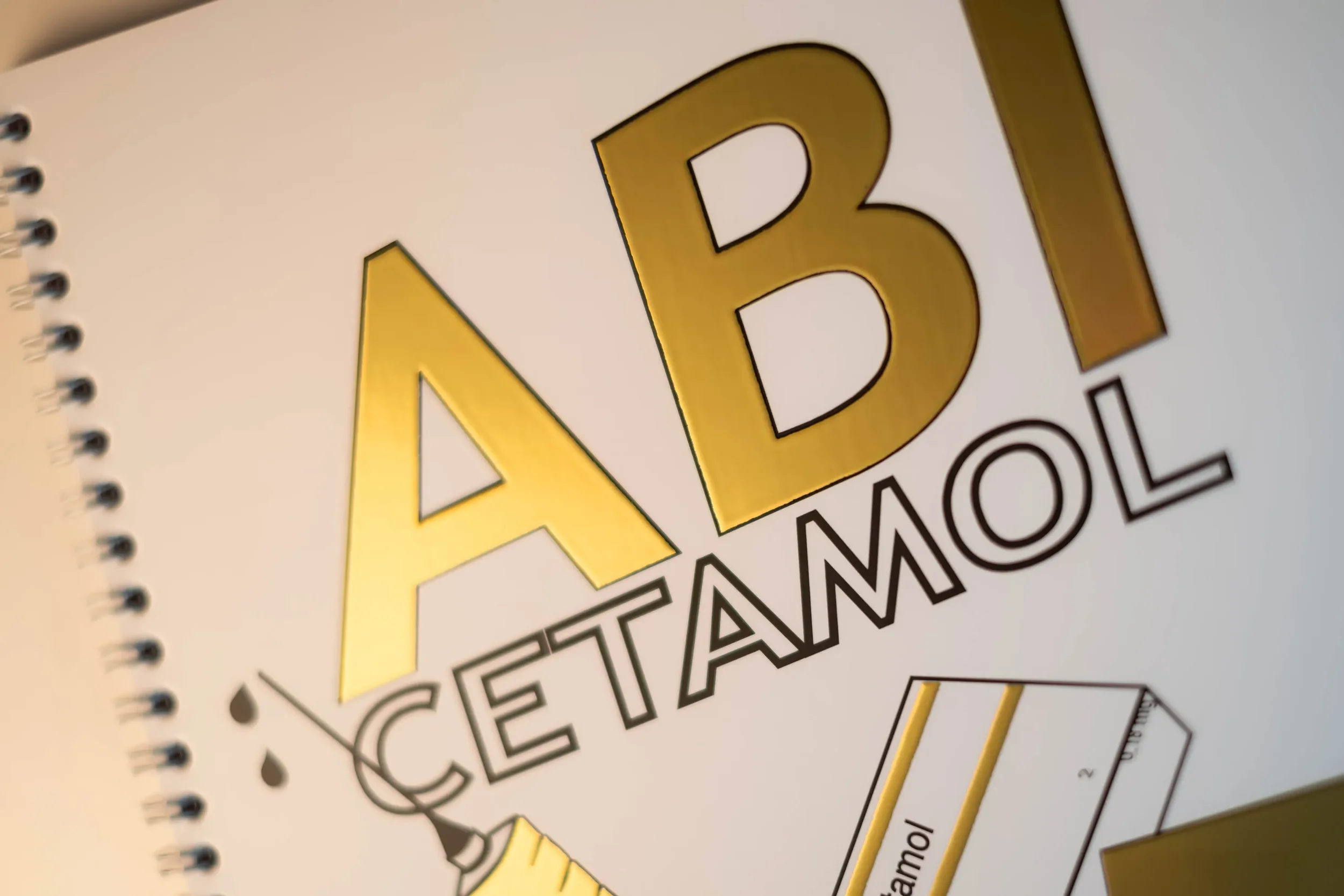 Gebuchtes Handbuch mit goldenen Buchstaben mit Schriftzug "ADAC Cetamol" und einem Stift auf weißem Hintergrund.