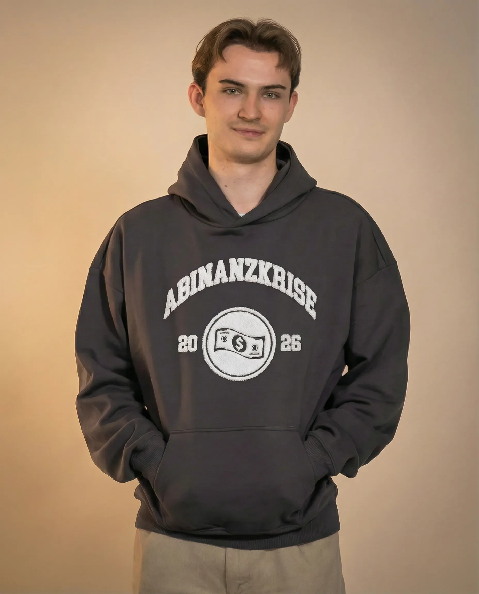 Junge trägt schwarze Kapuzenjacke mit Aufdruck "AbinzKabisze" und Geldmünzen-Logo, beige Wand im Hintergrund.