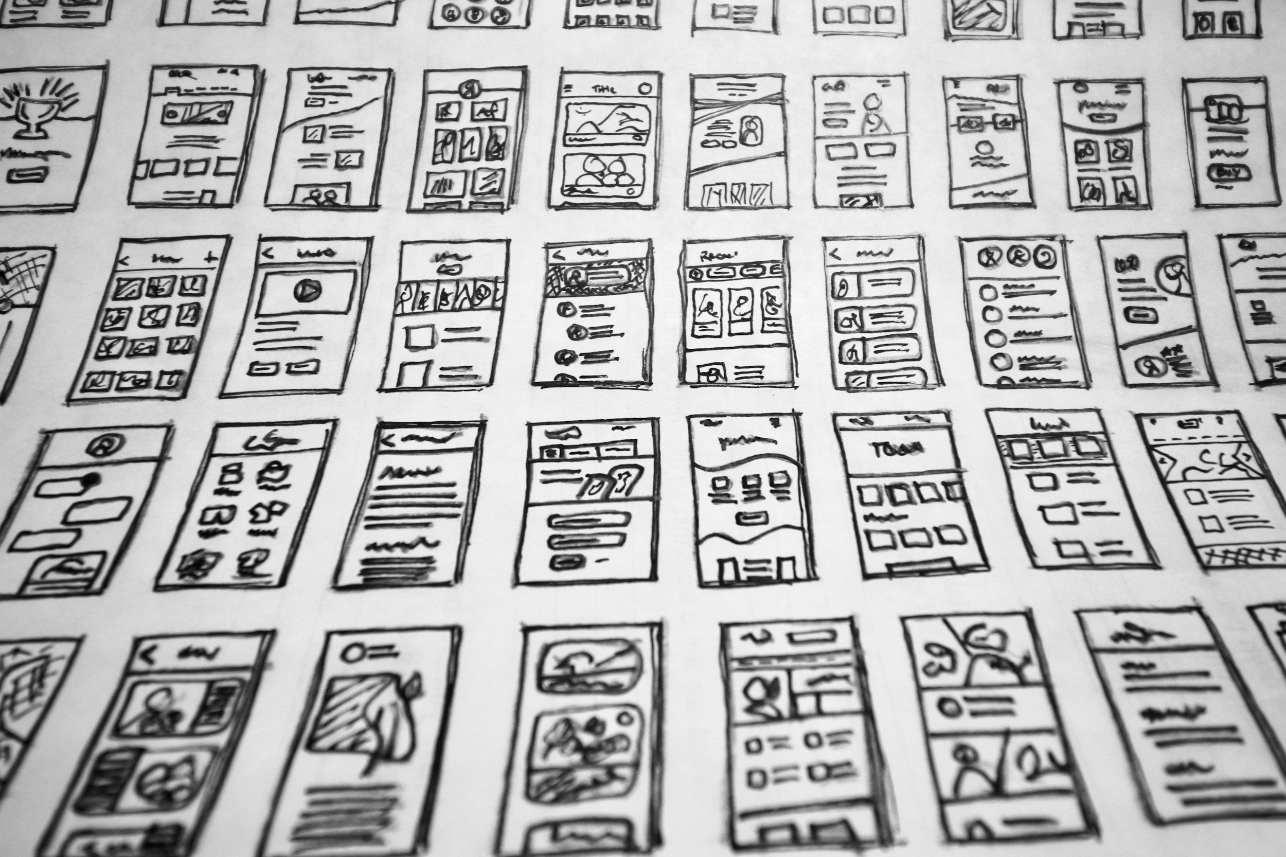 Sketches of multiple mobile app wireframes drawn on white paper, arranged in rows and columns.