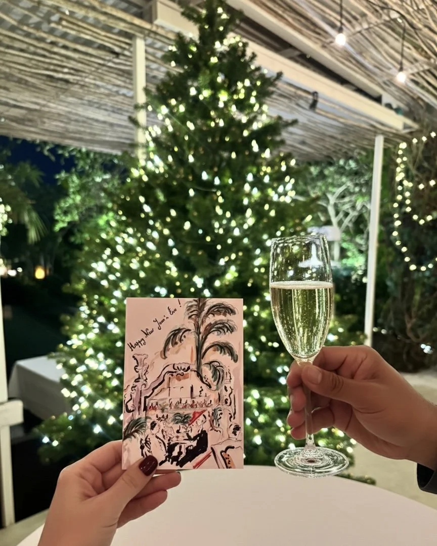 Celebrating Christmas with a decorated tree, a hand holding a greeting card with a festive illustration, and another hand holding a glass of champagne.