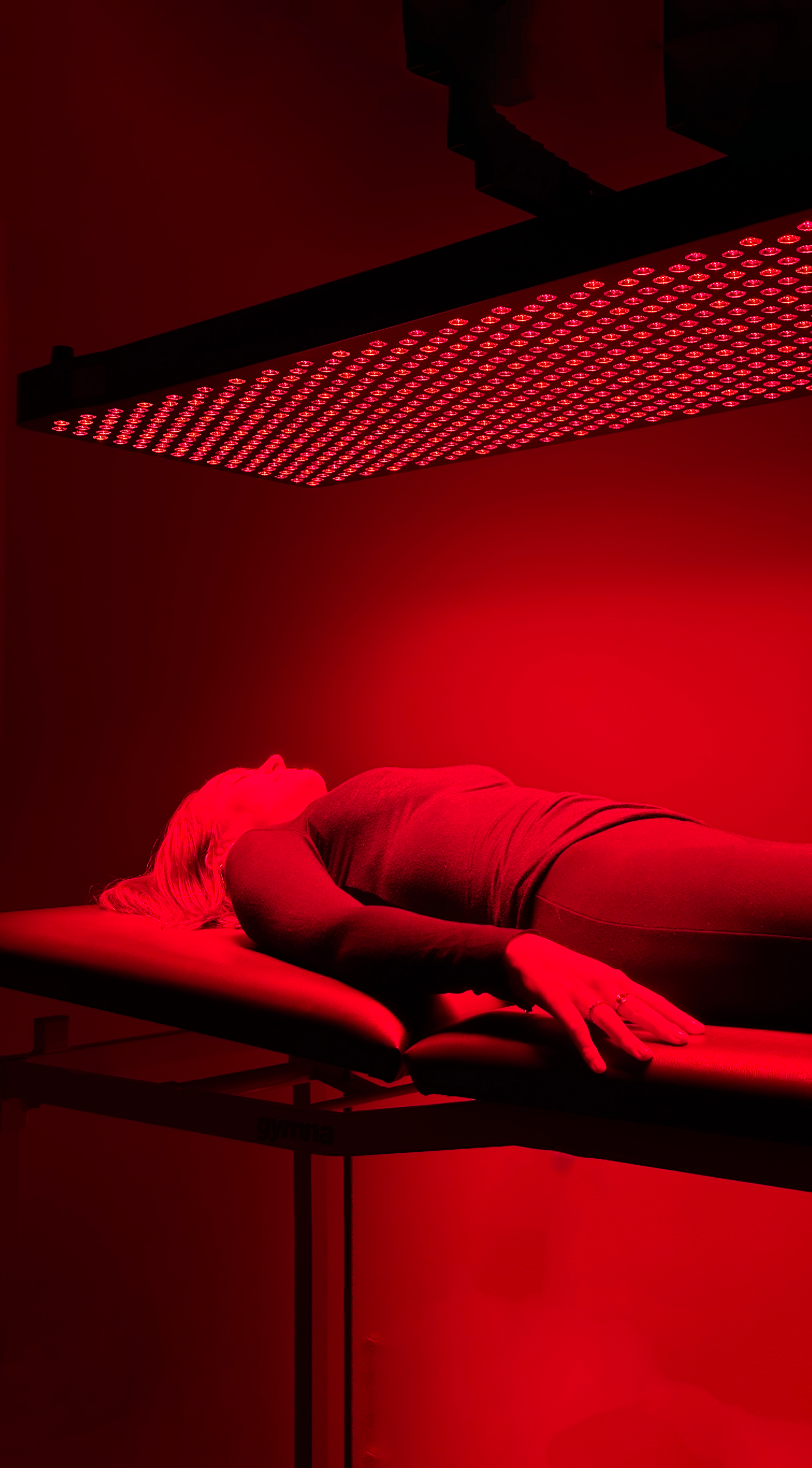 Une femme allongée sous une lampe de luminothérapie rouge dans une pièce sombre.