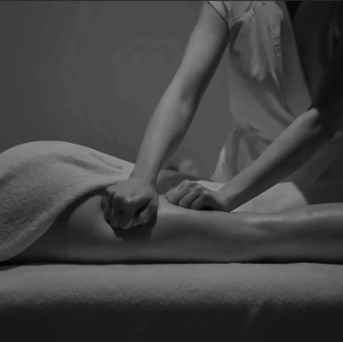 Une image floue d'une personne en mouvement, portant un pantalon sombre et une veste claire, tenant un tambour. Le fond est blanc.