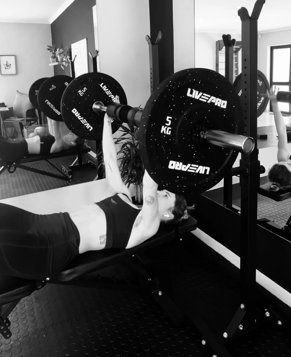 A woman lifting a barbell with weights while lying on a bench in a gym.