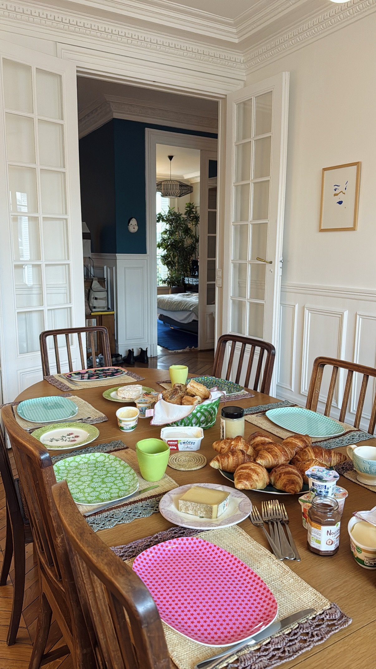 Morgenbord med croissanter, ost, yoghurt, brød, krydderurter, kaffe, mælk, spredt over et træbord i en spisestue.