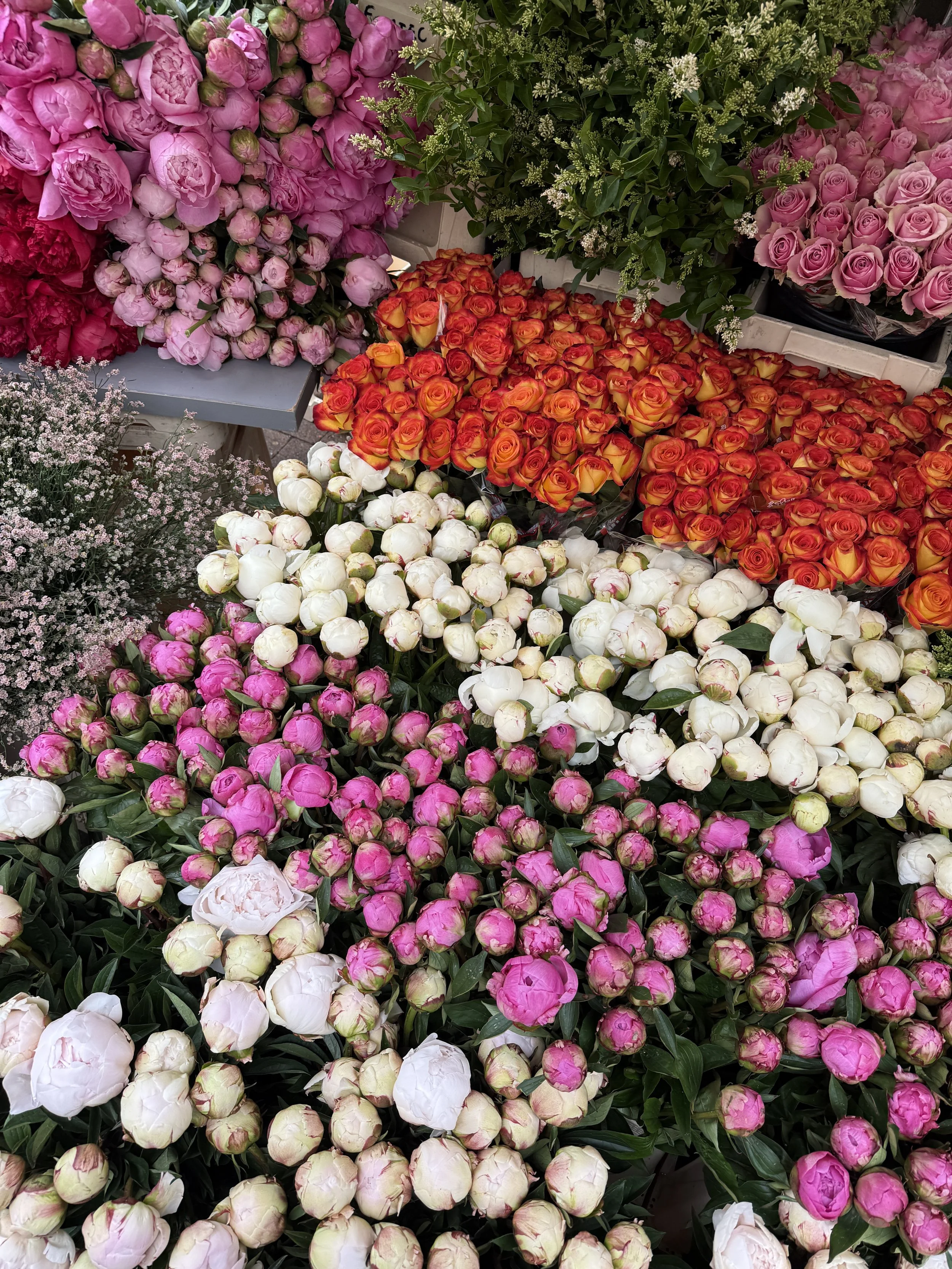 Et blomstermarked med forskellige farverige buketter og blomster, herunder pink, rød, orange, hvid og lilla blomster.