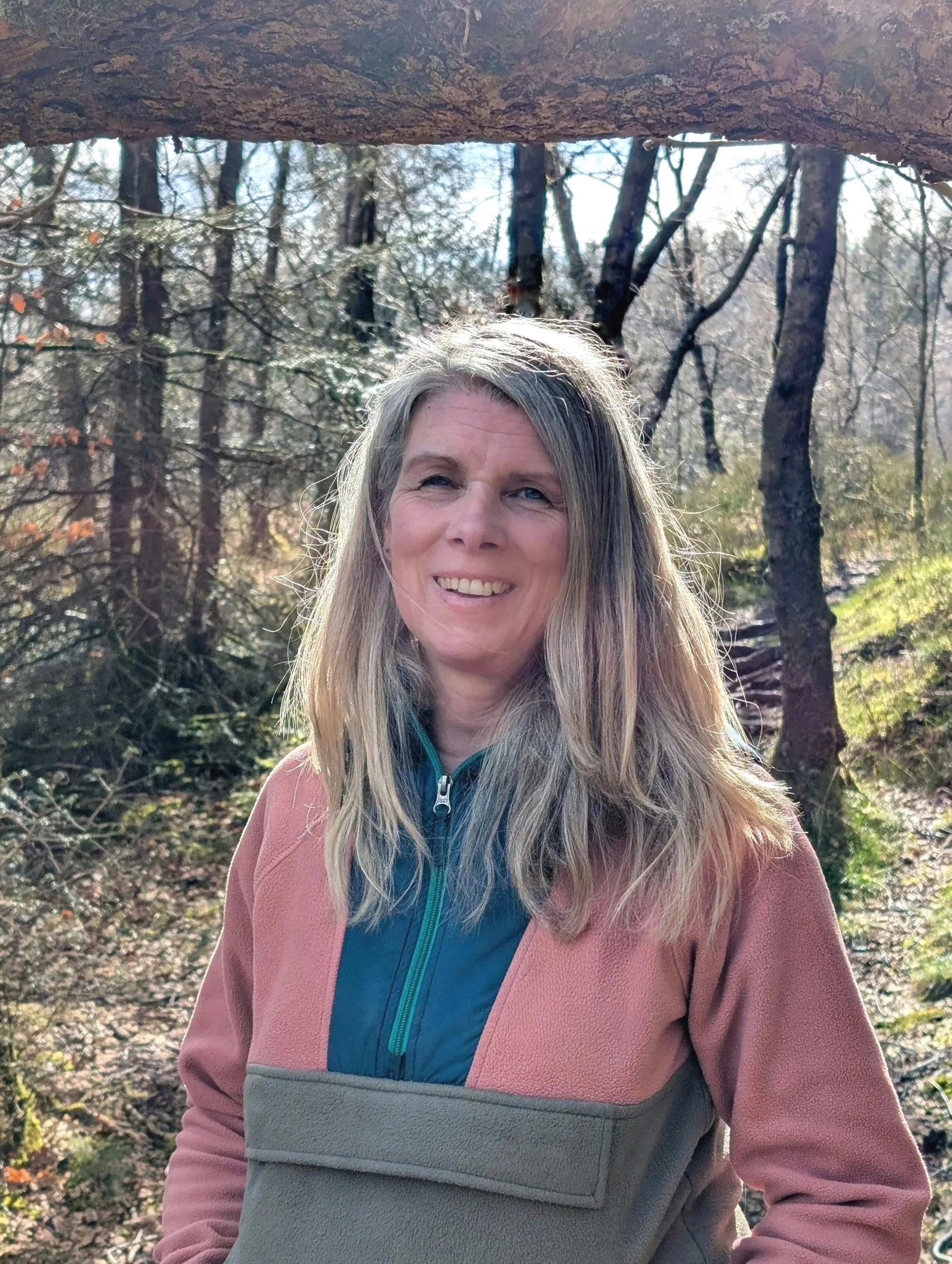 Rachael from Rachael Beecham Counselling, smiling outdoors in a wooded area with trees and sunlight in the background.