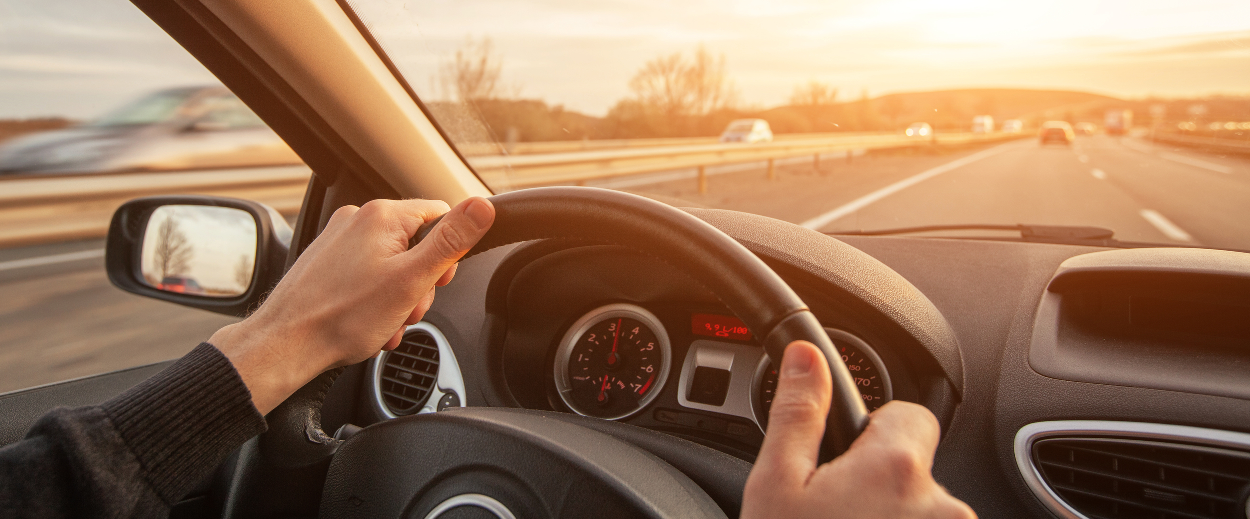 Person kjører bil på motorvei i solnedgang